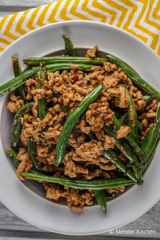 Ground turkey stir fry with green beans in a spicy sauce with a white plate and yellow napkin.