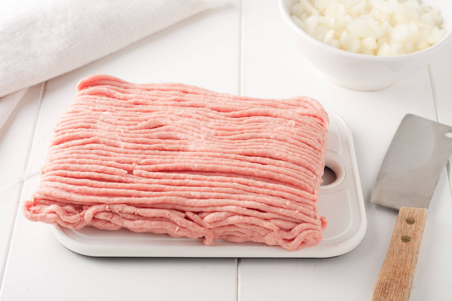 Ground turkey on a cutting board with an onion and knife.