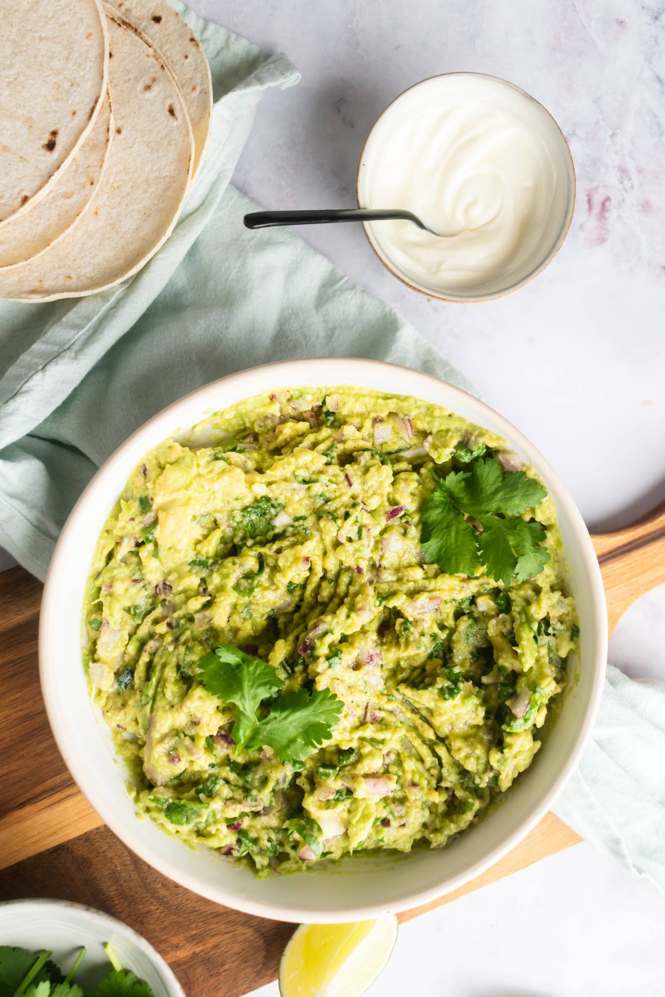 Homemade guacamole with avocados, cilantro, jalapeno, and lime juice in a bowl with tortillas on the side.