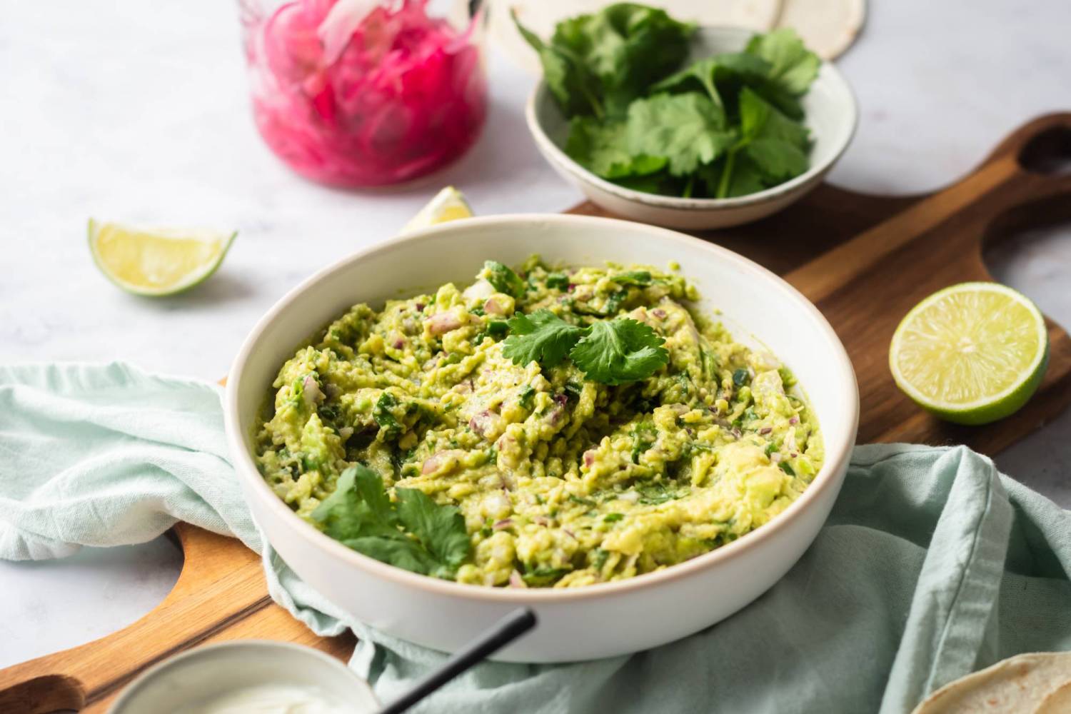 Authentic guacamole served in a bowl with avocado, limes, cilantro, red onion, and salt.