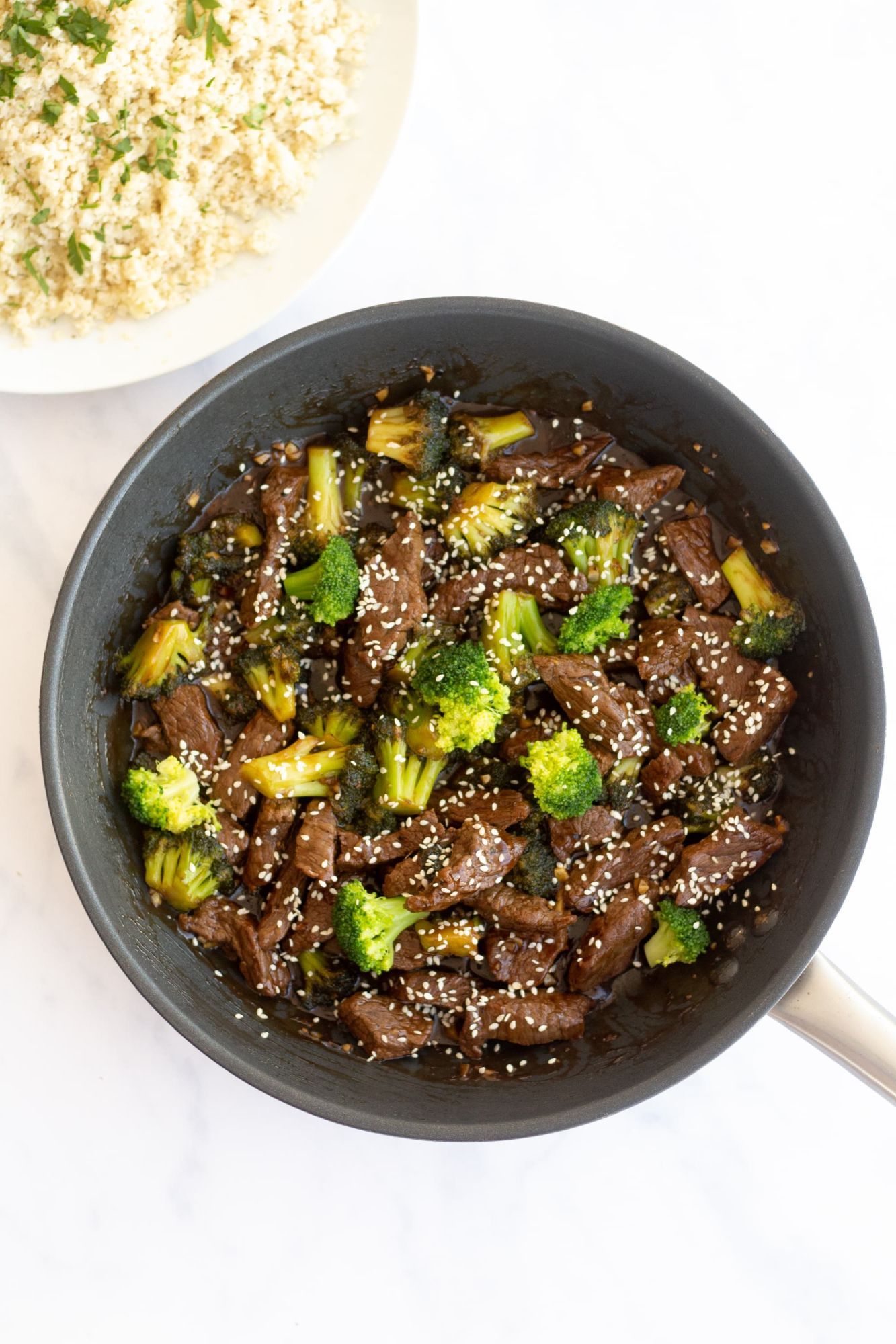 Chinese beef and broccoli served in a bowl with rice, green broccoli, sliced steak, and sesame seeds.