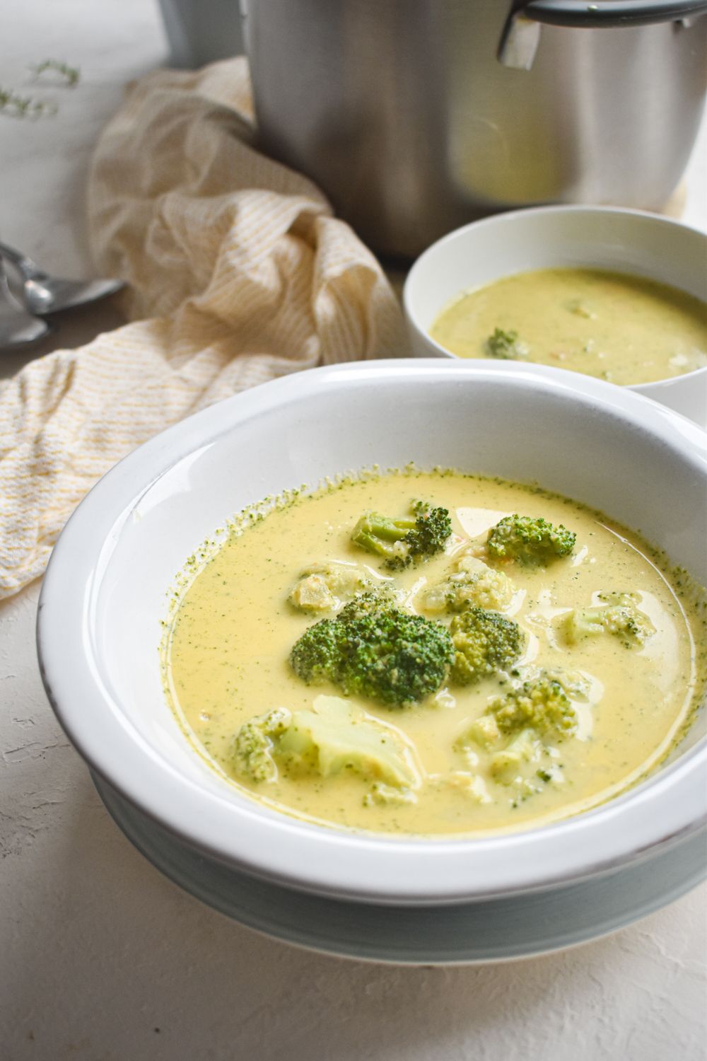 Broccoli cheese soup with a cheddar cheese broth and broccoli florets in two bowls with a yellow napkin.