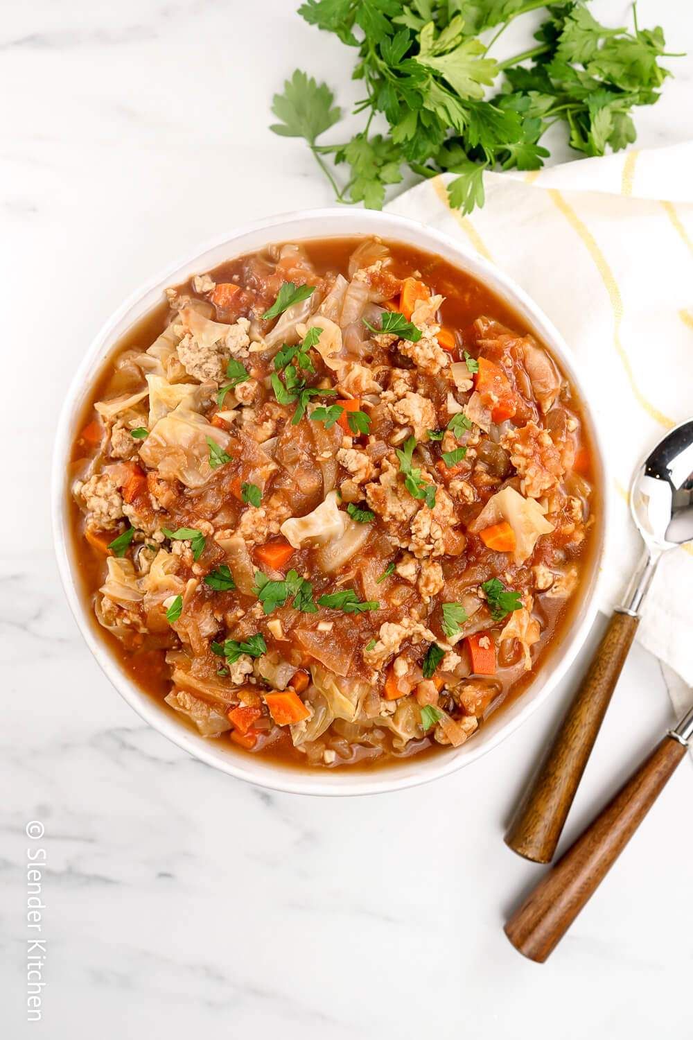 Cabbage soup in a wooden bowl with fresh parsley and two spoons.