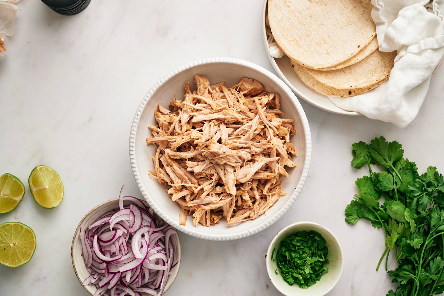 Ingredients for healthy carnitas tacos including shredded pork carnitas, cilantro, onion, and tortillas.