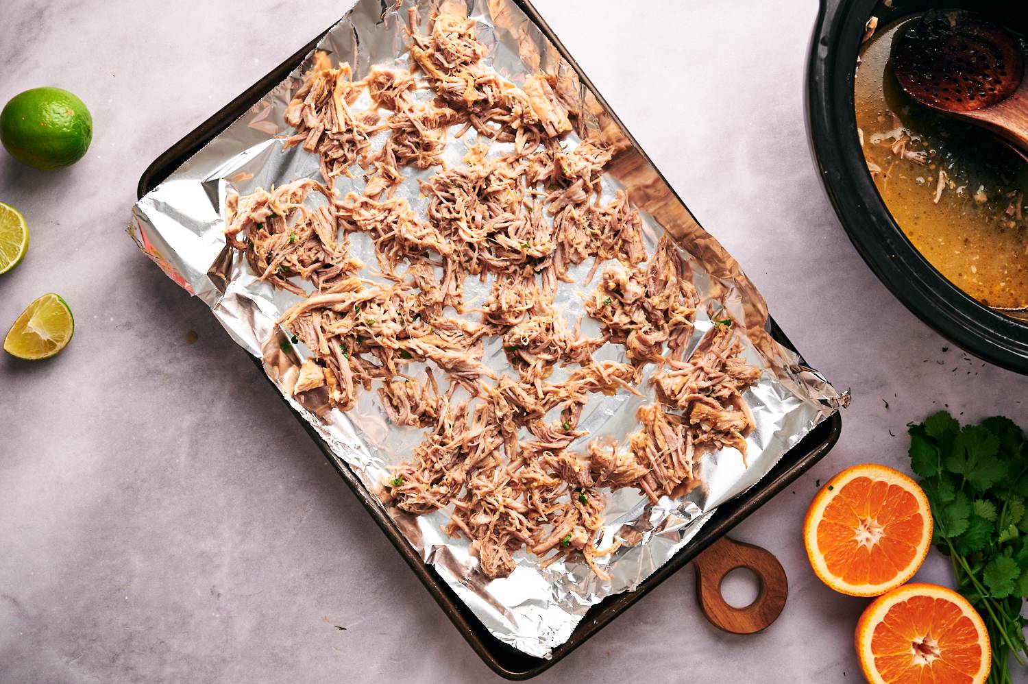 Pork carnitas tacos shredded on a baking sheet with a slow cooker on the side.