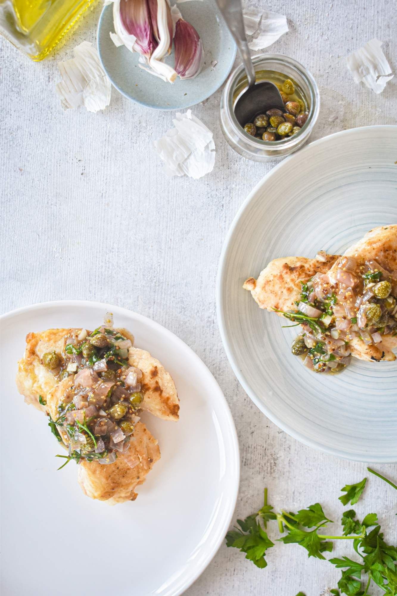 Chicken piccata with capers, shallots, and a butter garlic sauce on a plate with parsley on the side. 