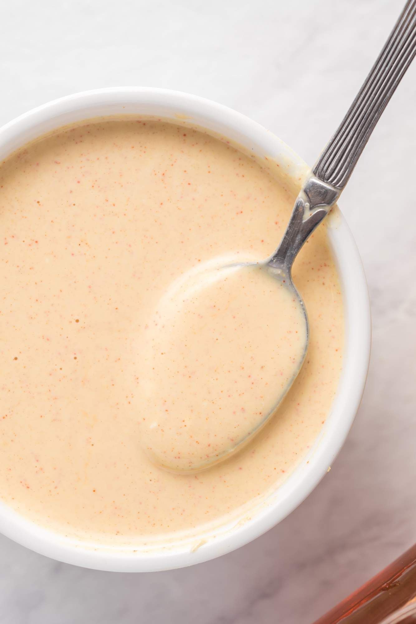 Yogury honey mustard dressing in a bowl with Greek yogurt, mustard, and honey mixed with paprika.