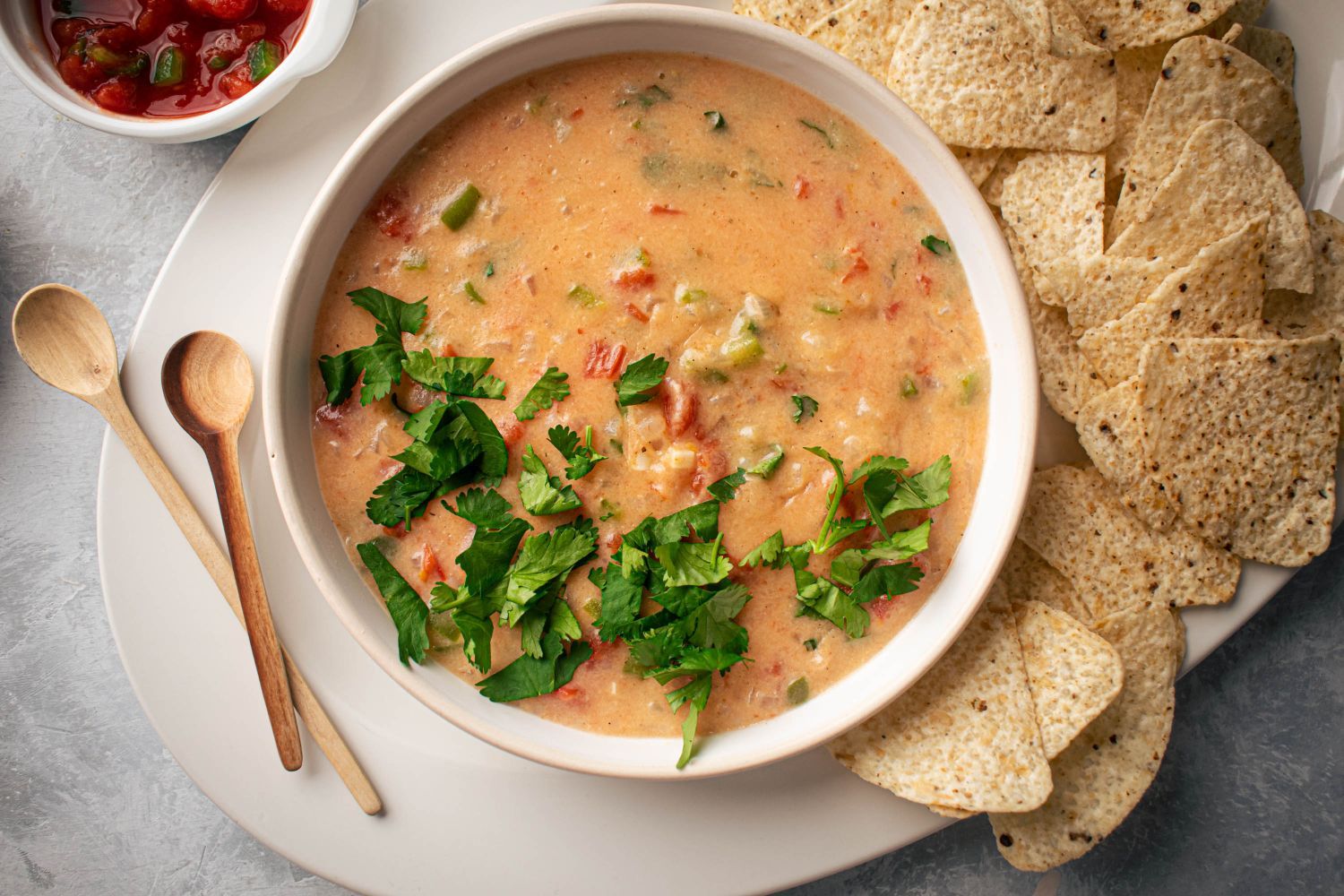 Queso dip with tomatoes, onions, and cheddar cheese served in a bowl with chips.