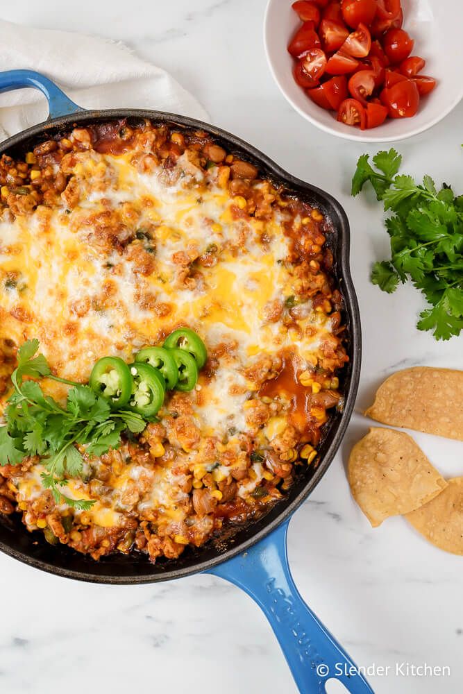 Healthy taco casserole in a cast iron skillet with melted cheese, beans, ground turkey, and salsa.