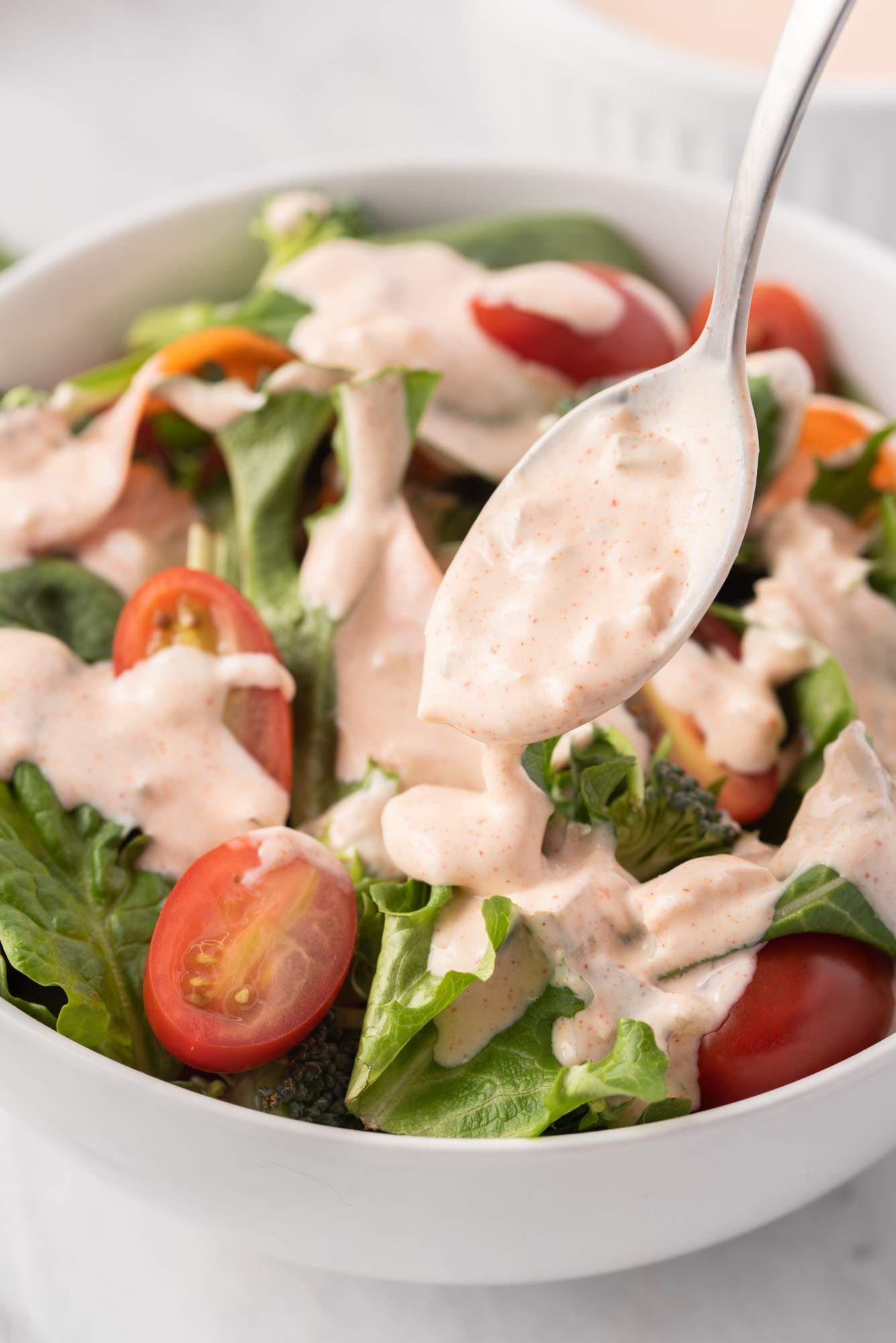 Green salad with thousand island dressing being poured over top and drizzled with a spoon.