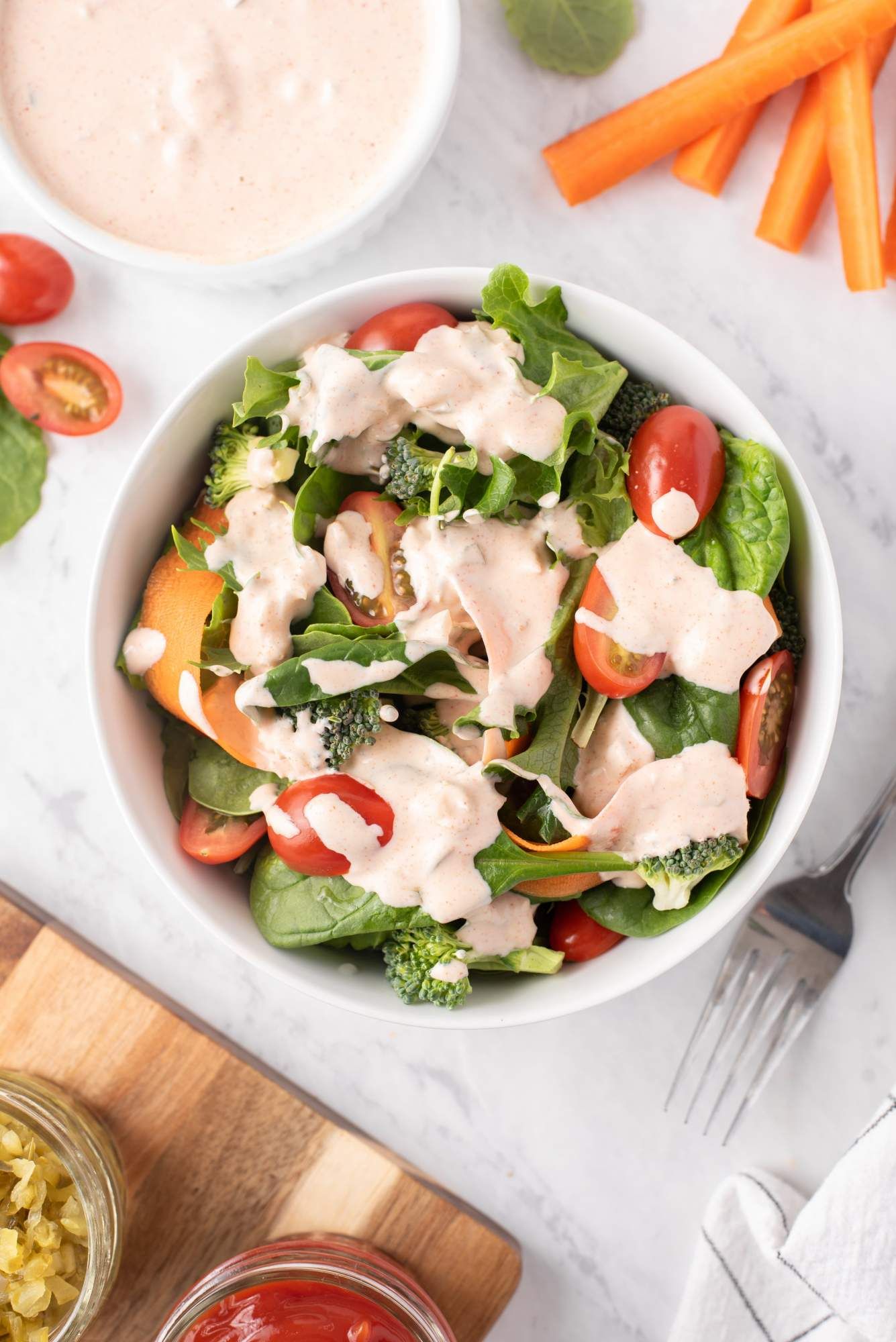 Thousand island yogurt dressing served on a green salad with tomatoes, carrots, and greens.