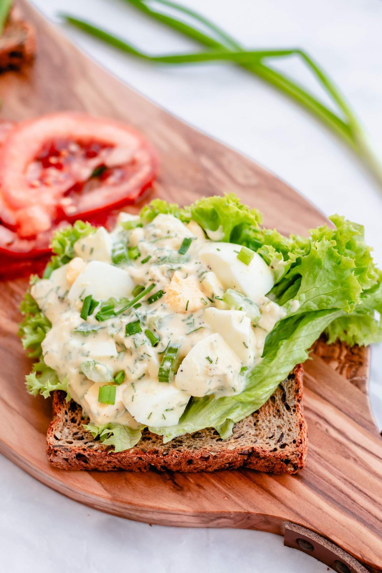 Greek yogurt egg salad with fresh herbs and hard boiled eggs on whole wheat bread with tomato and lettuce.