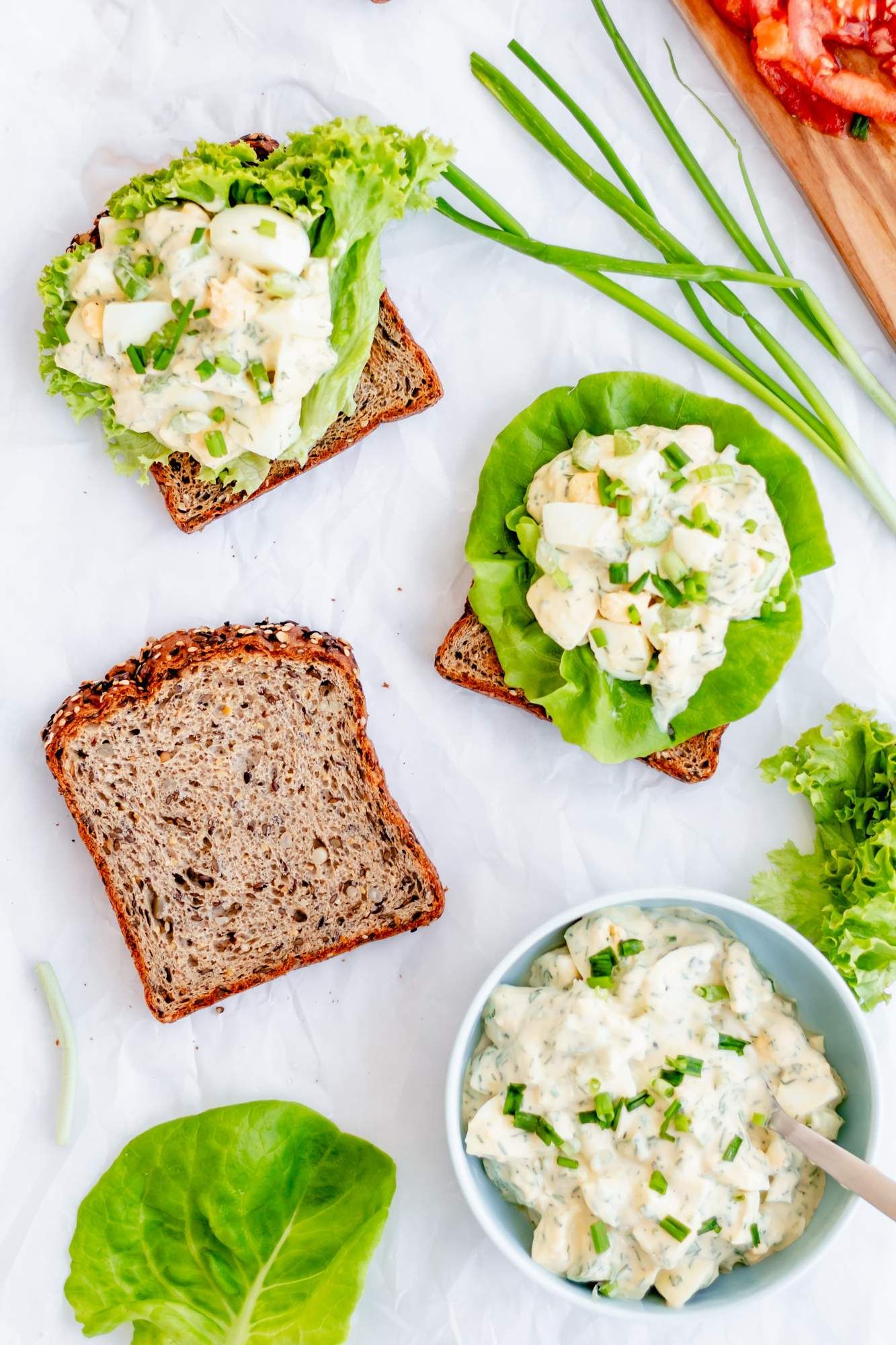 Healthier herb egg salad made with Greek yogurt served with lettuce and tomato on wheat bread slices.