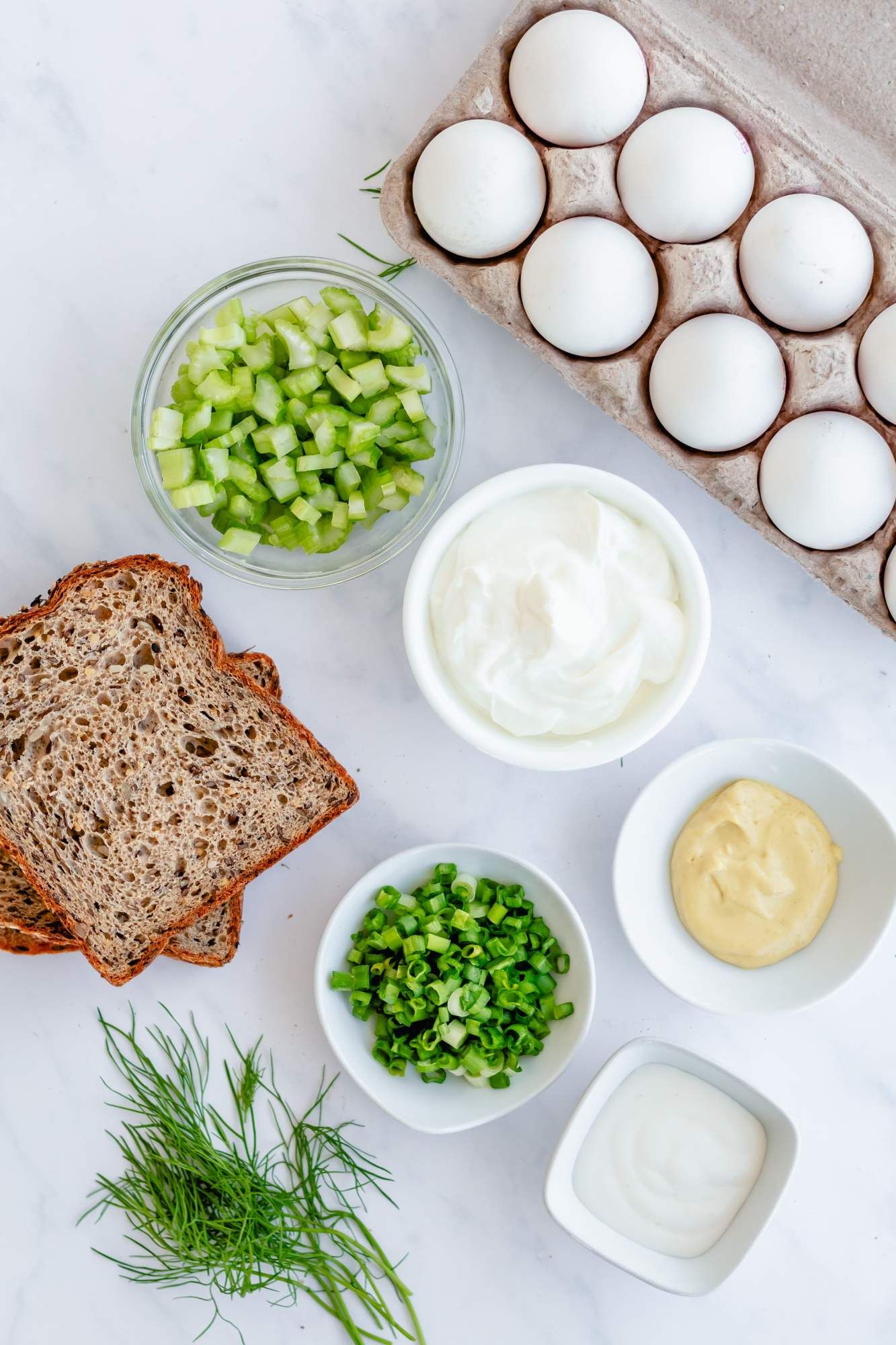 Ingredients for healthy egg salad including boiled eggs, Greek yogurt, mayonnaise, mustard, and fresh herbs,