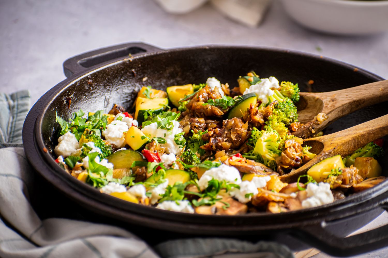 Vegetable hash with potatoes, zucchini, bell peppers, and broccoli with two wooden spoons.