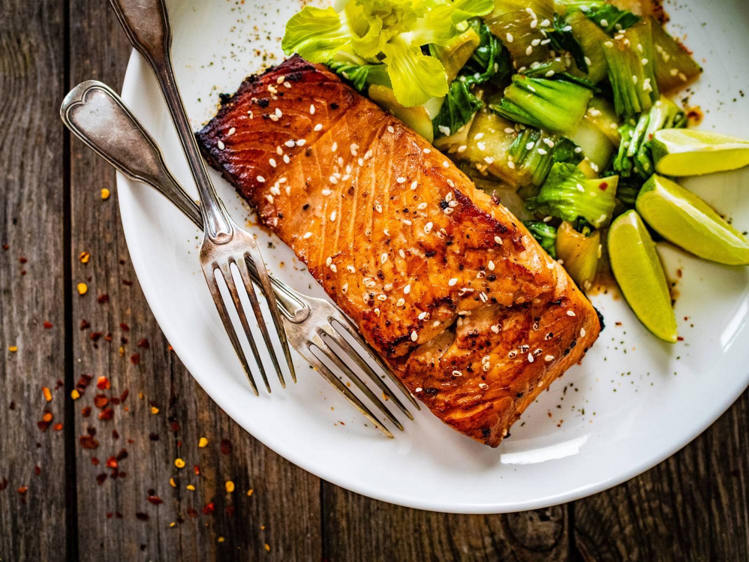 Asian hoisin glazed salmon on a plate with sauteed bok choy and limes. 