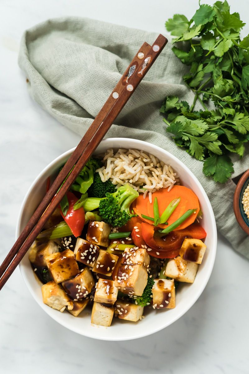 Tofu bowls with broccoli, carrots, celery, red peppers, and brown rice drizzled with hoisin sauce.