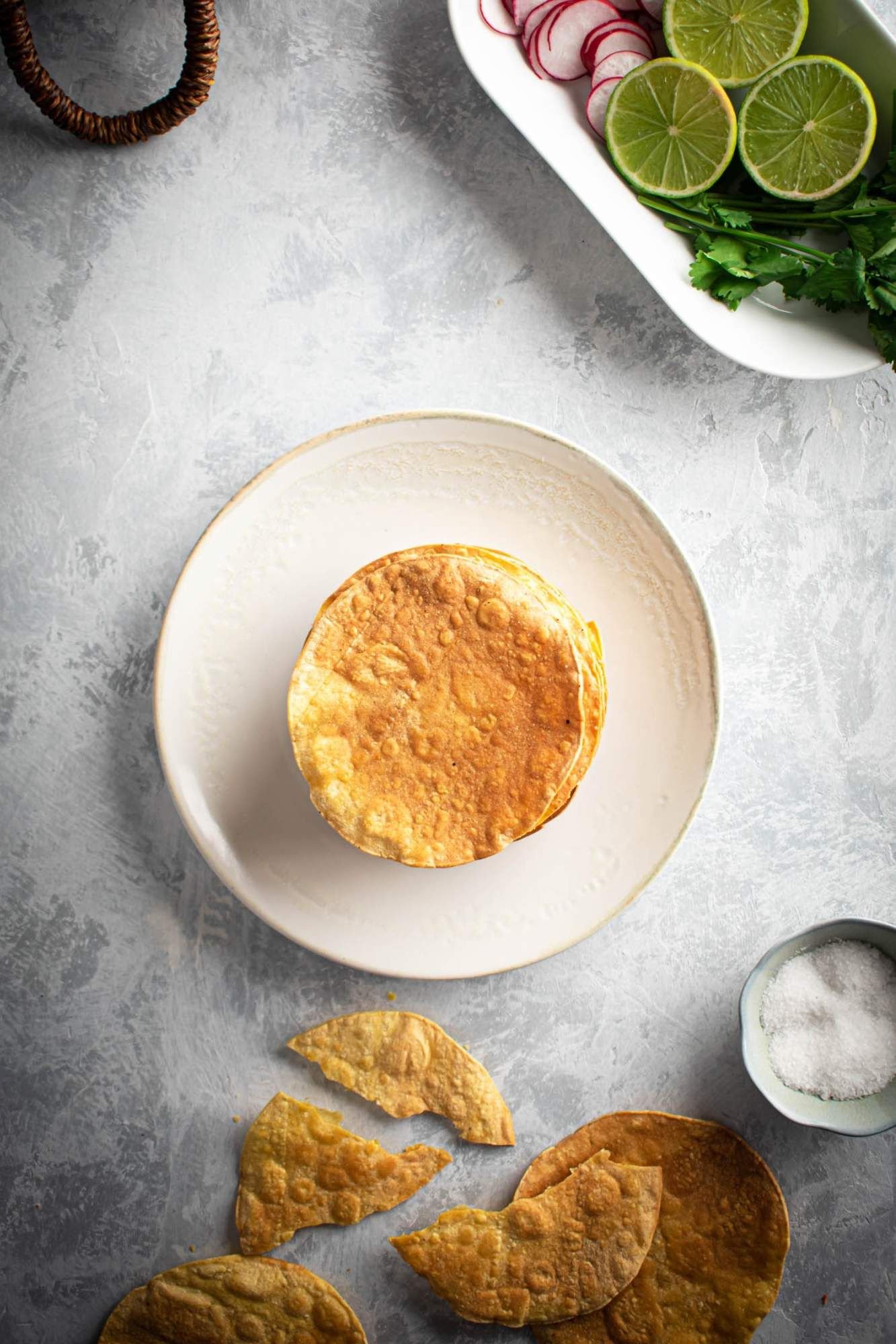 Baked tostada shells with crispy corn tortillas in a pile with limes an cilantro on the side.