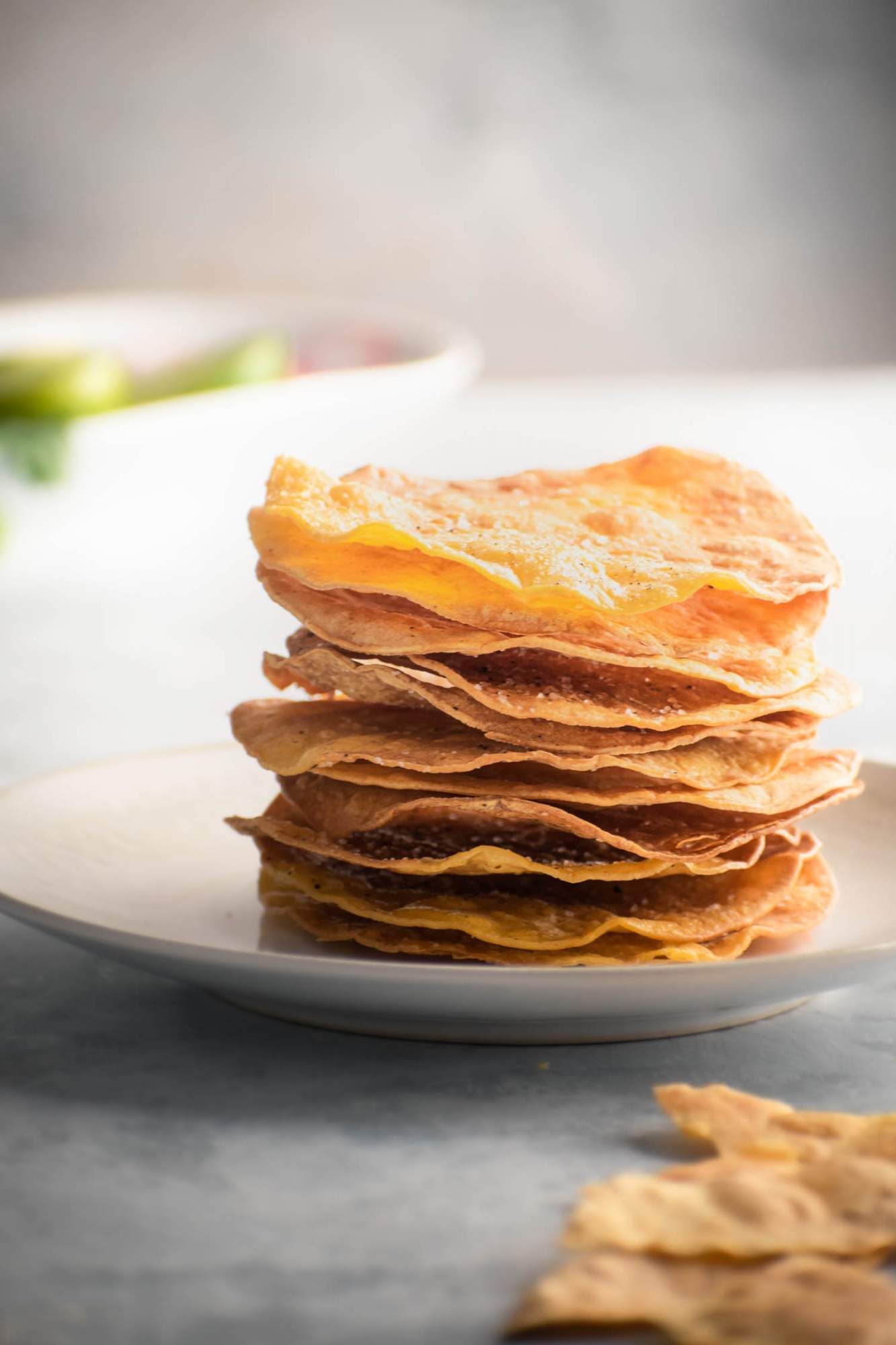 Homemade tostadas made with corn tortillas, salt, pepper, and oil stacked on a plate with limes on the side.