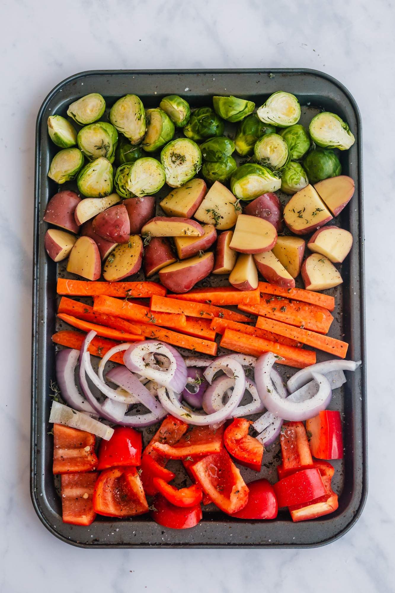 Vegetables on a baking sheet with olive oil, salt, pepepr, and herbs.