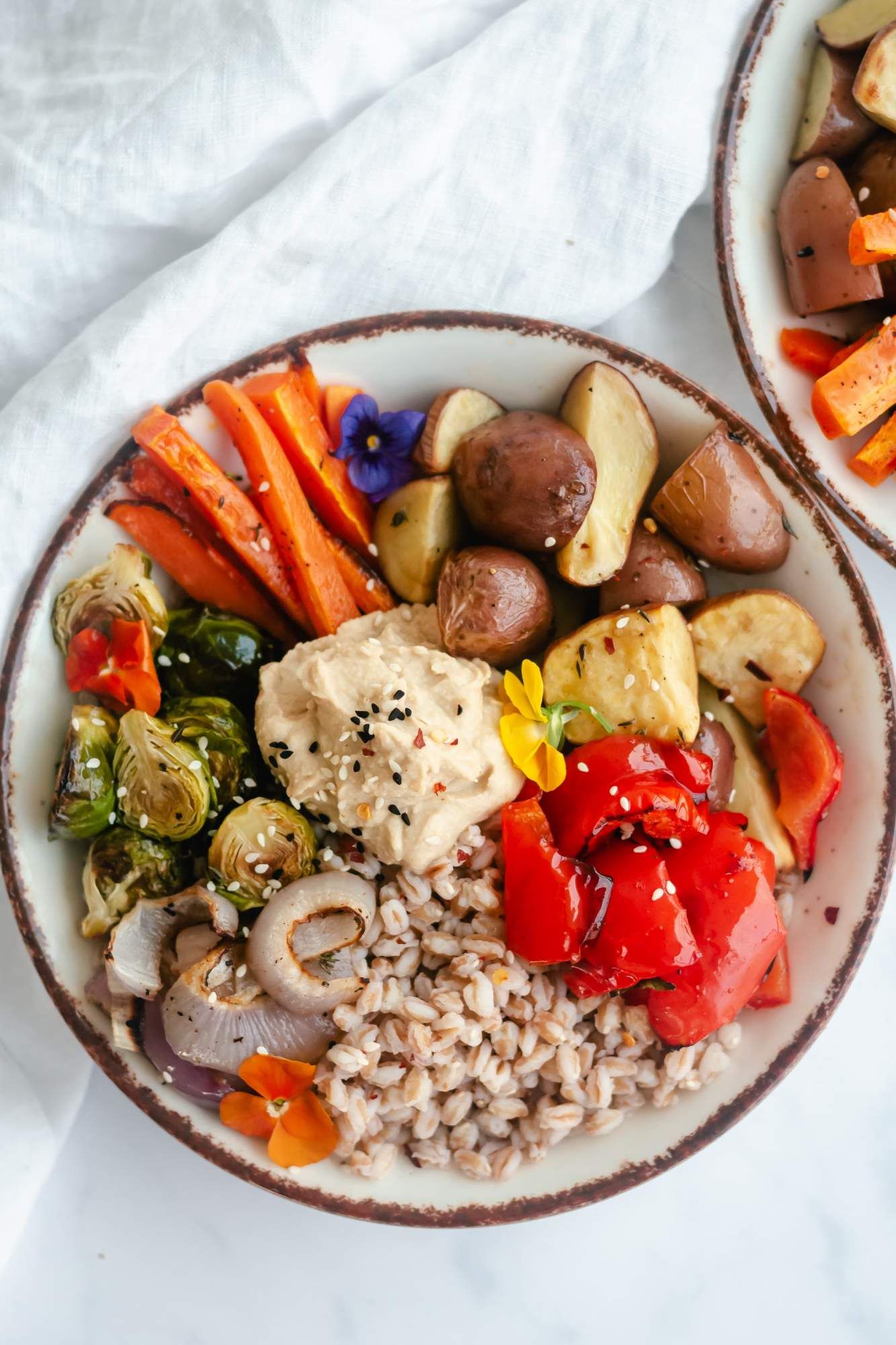 Roasted vegetable and farro bowls with carrots, potatoes, Brussels sprouts, peppers, onions, and farro in a bowl with hummus.