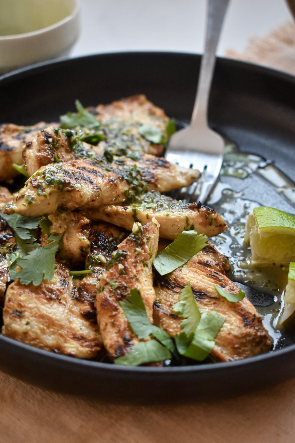 Grilled honey lime chicken on a plate with fresh limes, chopped cilantro, and a fork.