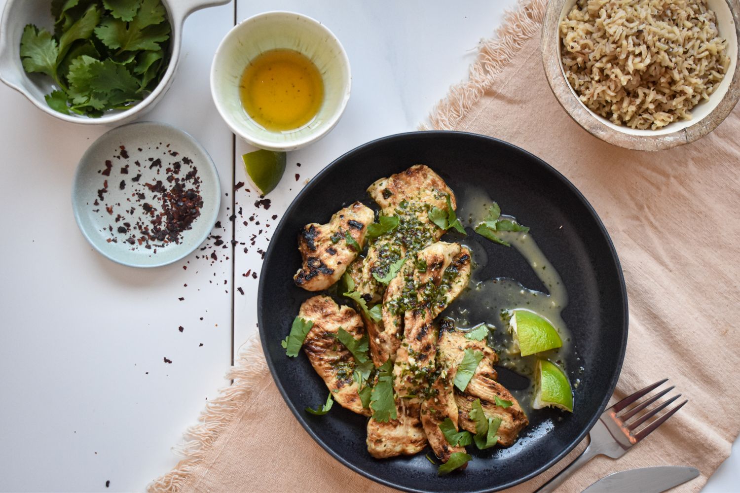 Grilled chicken with honey lime marinade on a plate with honey, red pepper flakes, cilantro, and brown rice on the side.