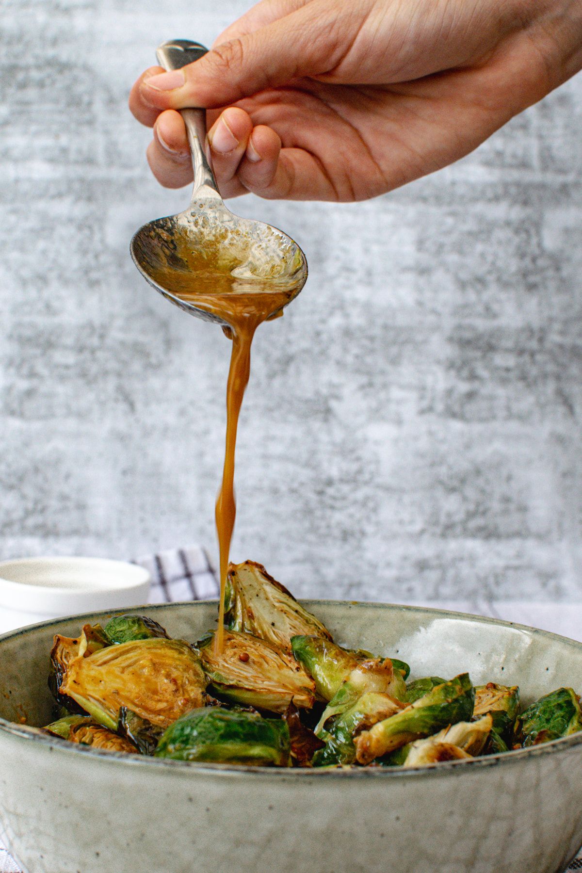 Roasted Brussels sprouts with honey mustard sauce being drizzled on top with a spoon.