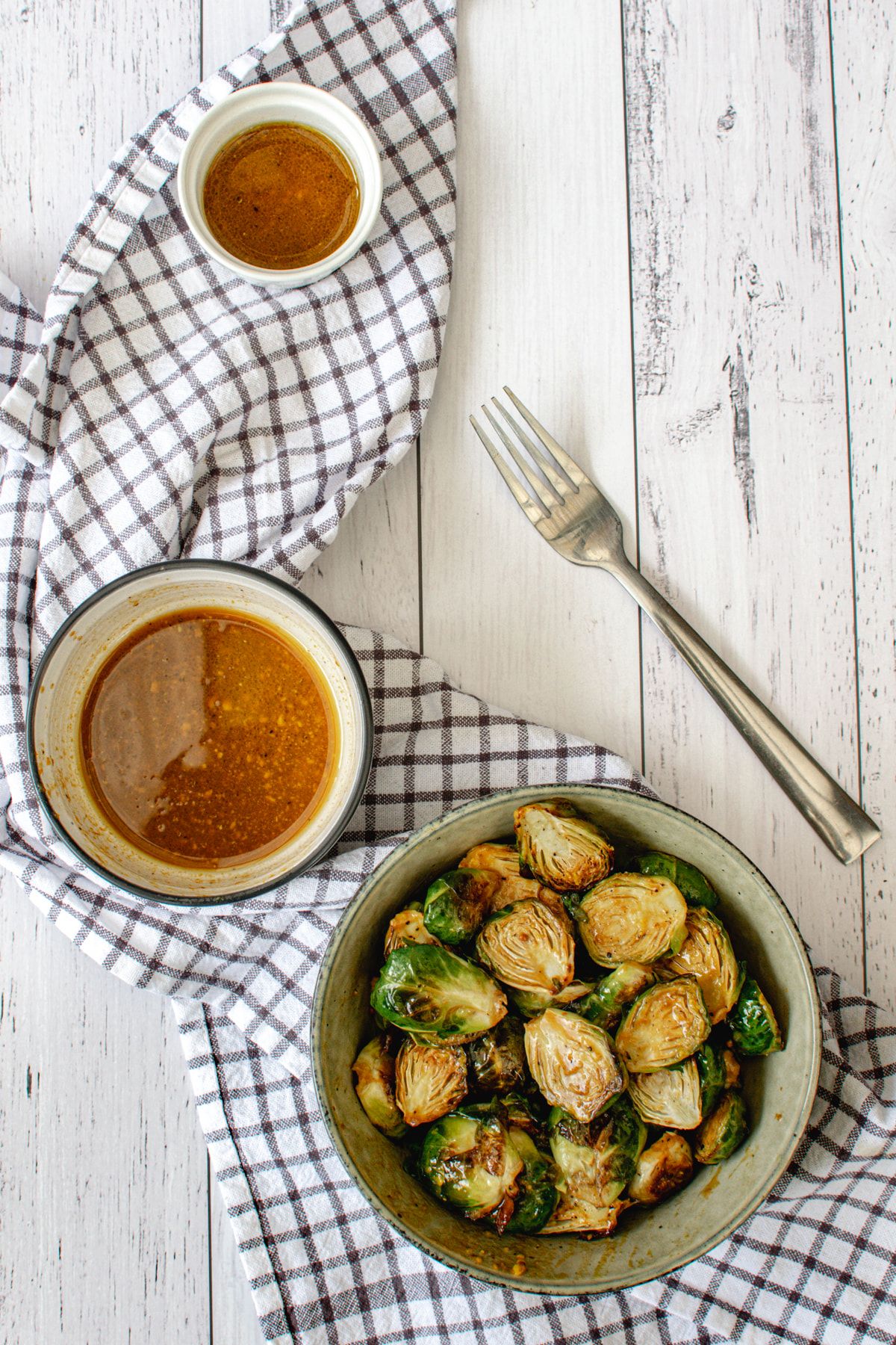 Mustard Brussels sprouts in a bowl with a checked napkin and small bowl of honey mustard sauce on the side.