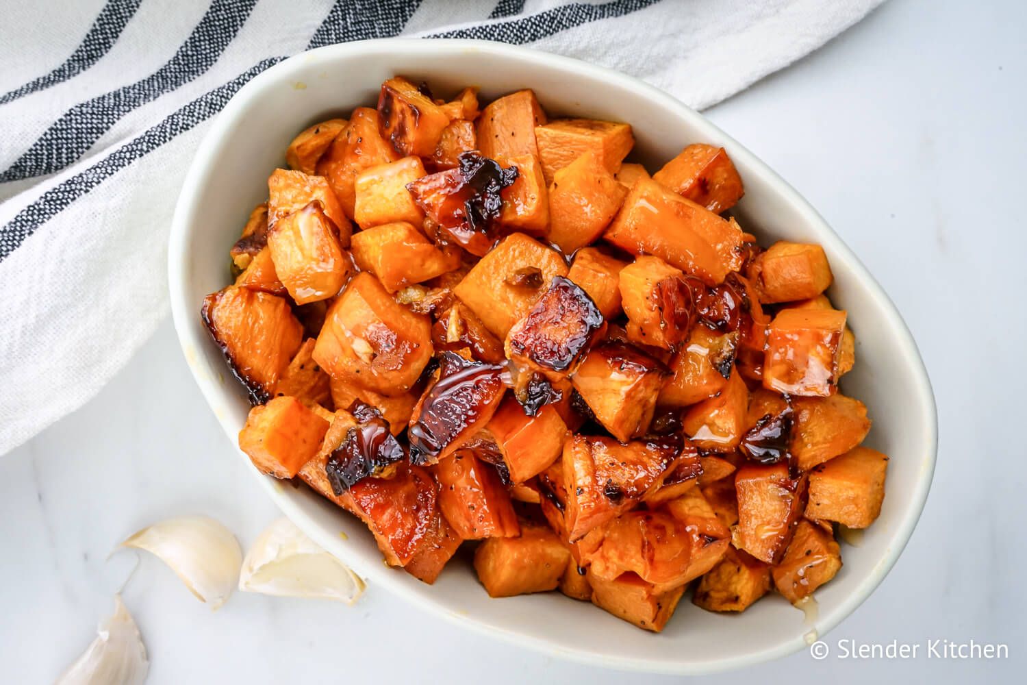 Honey roasted sweet potatoes with garlic in a dish with caramelized browned edges.