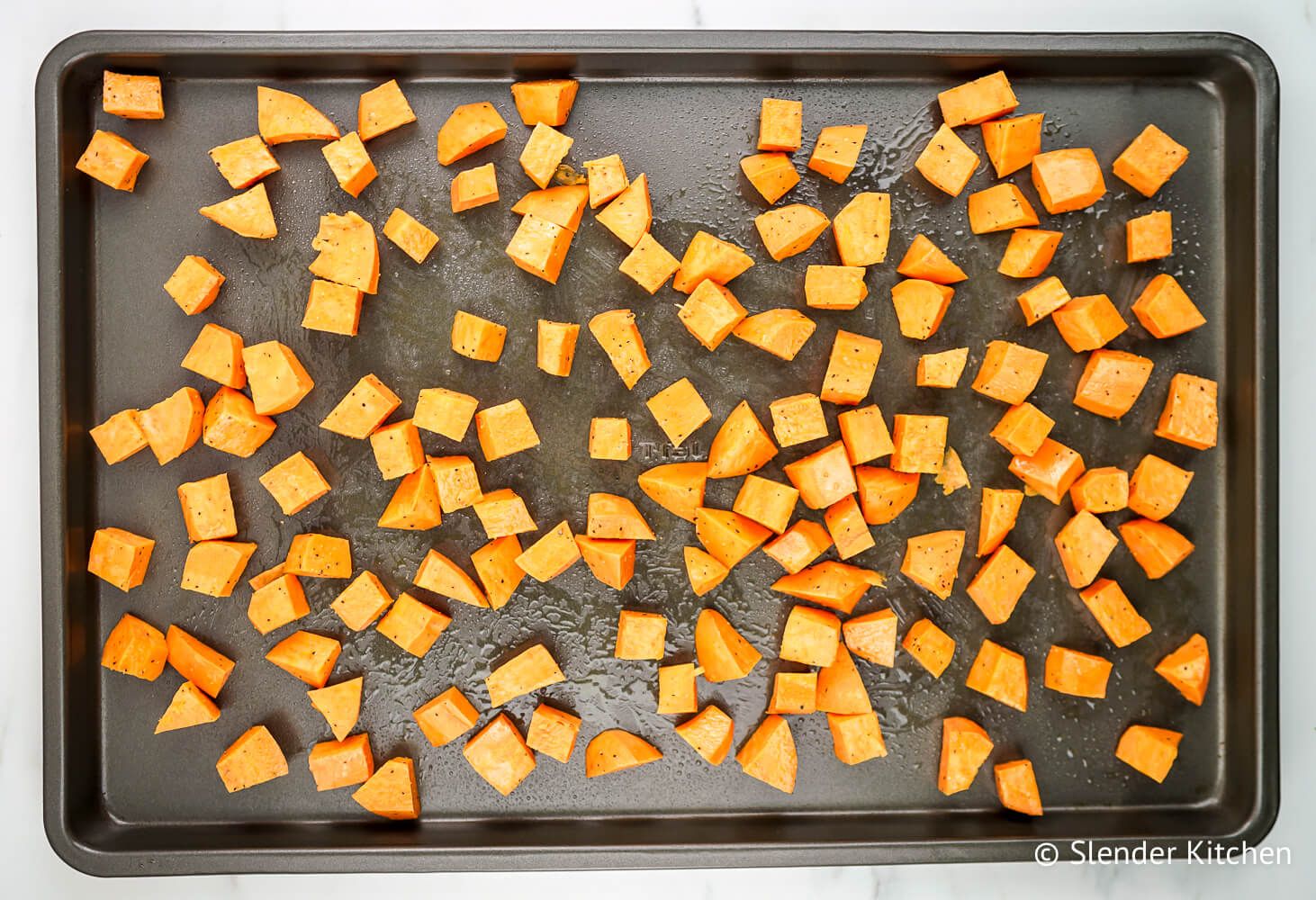 Sweet potatoes on a baking sheet before being roasted with olive oil, salt, and pepper.