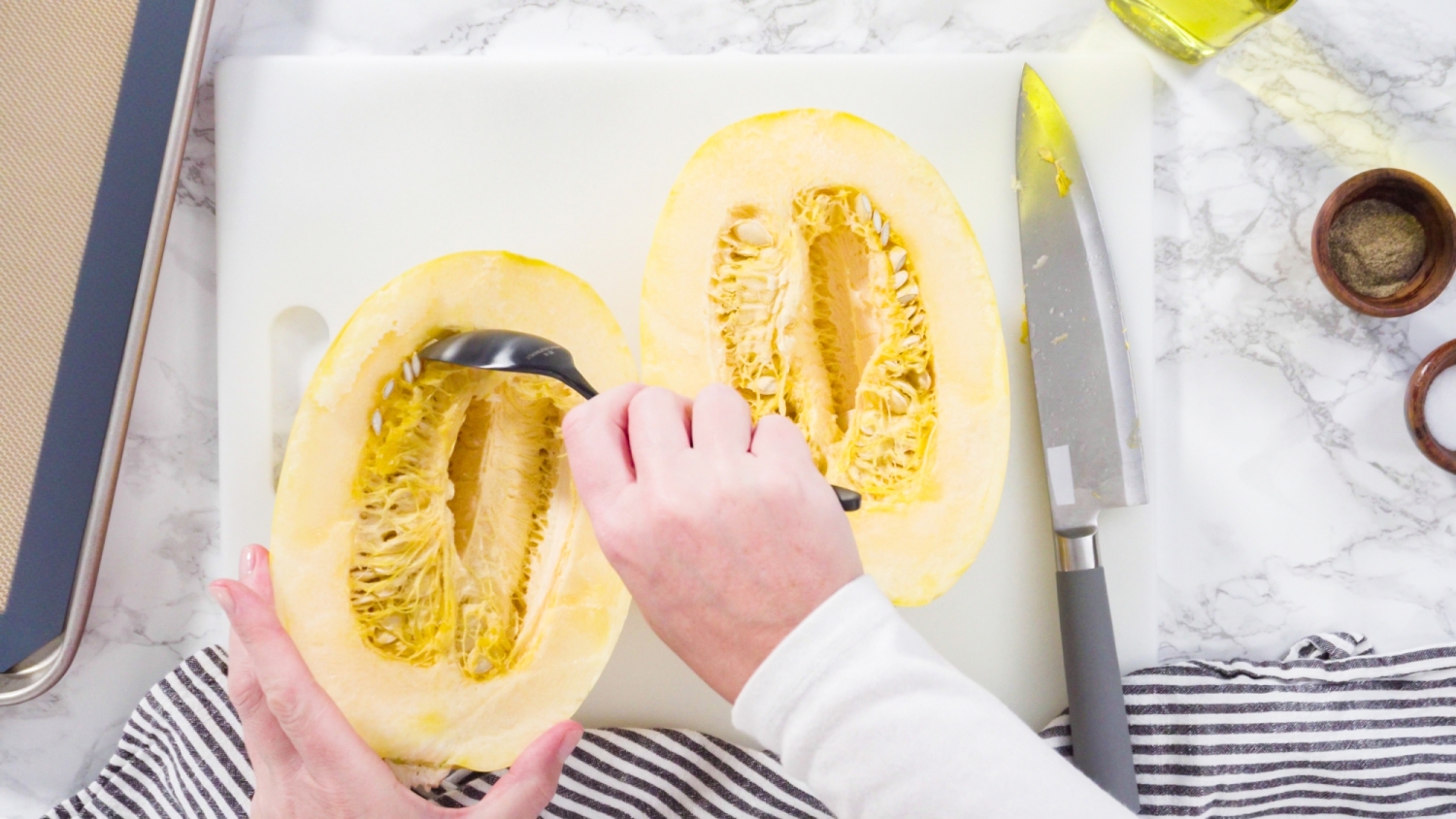 Spaghetti squash cut in half with someone scooping out the seeds.