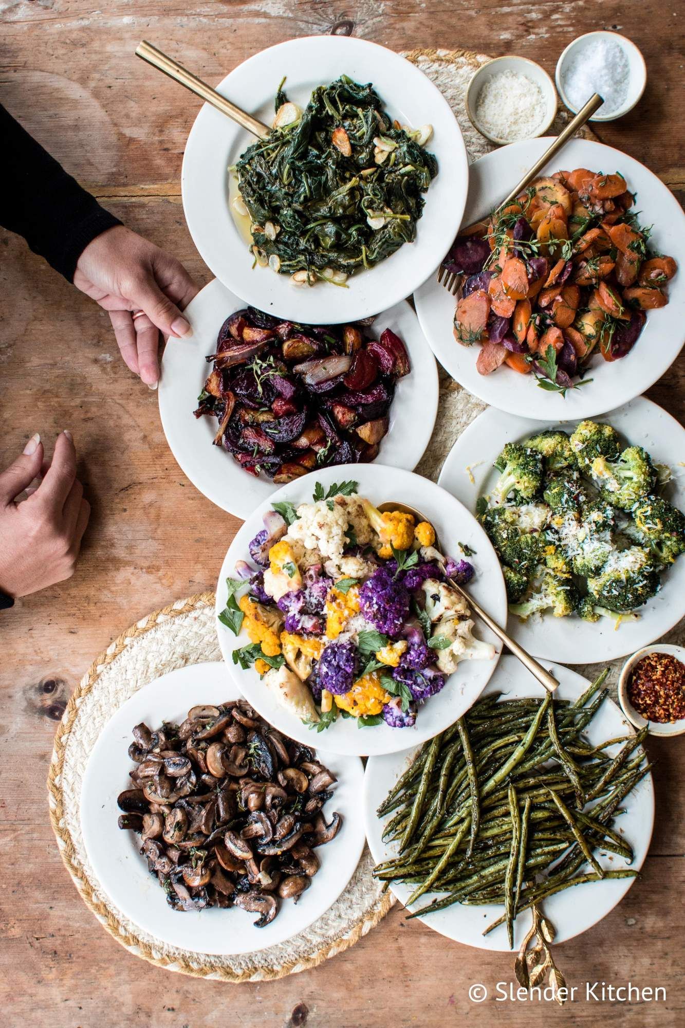 Various oven roasted vegetables including beets, bok choy, green beans, and cauliflower on plates on a wooden table.