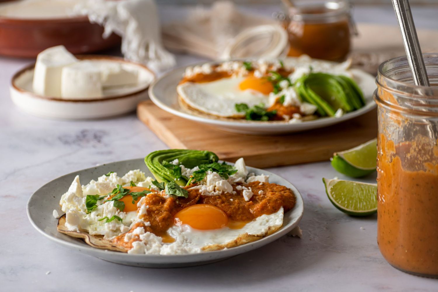 Homemade huevos rancheros served with avocado, ranchero sauce, queso fresco, and cilantro on two plates.