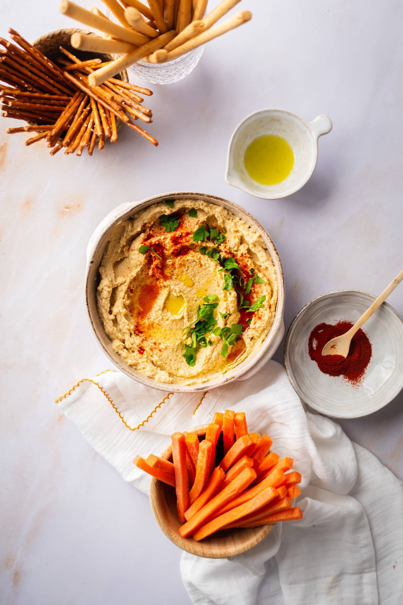 Chickpea hummus in a bowl served with carrots, pretzels, and breadsticks on the side.