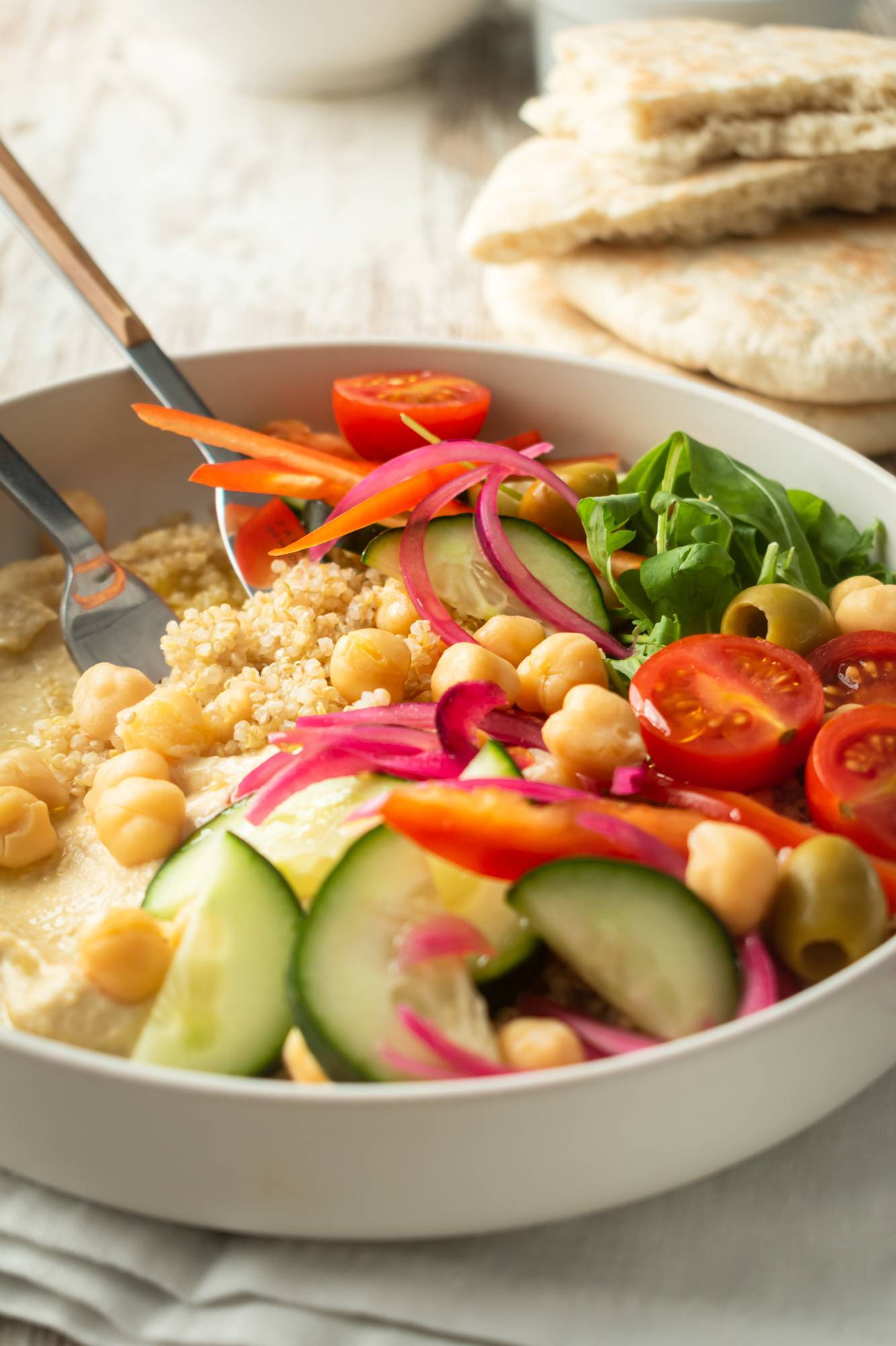 Hummus grain bowl with cucumbers, hummus, red onion, cherry tomatoes, arugula, and olives. 