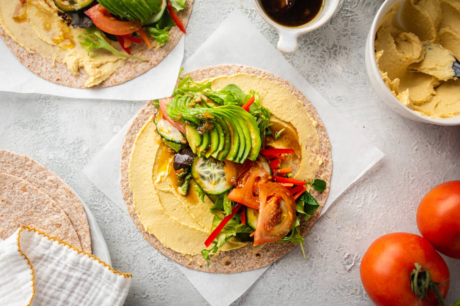 Hummus veggie wraps with hummus, greens, cucumbers, red bell peppers, tomatoes, and avocado on a whole grain wrap.