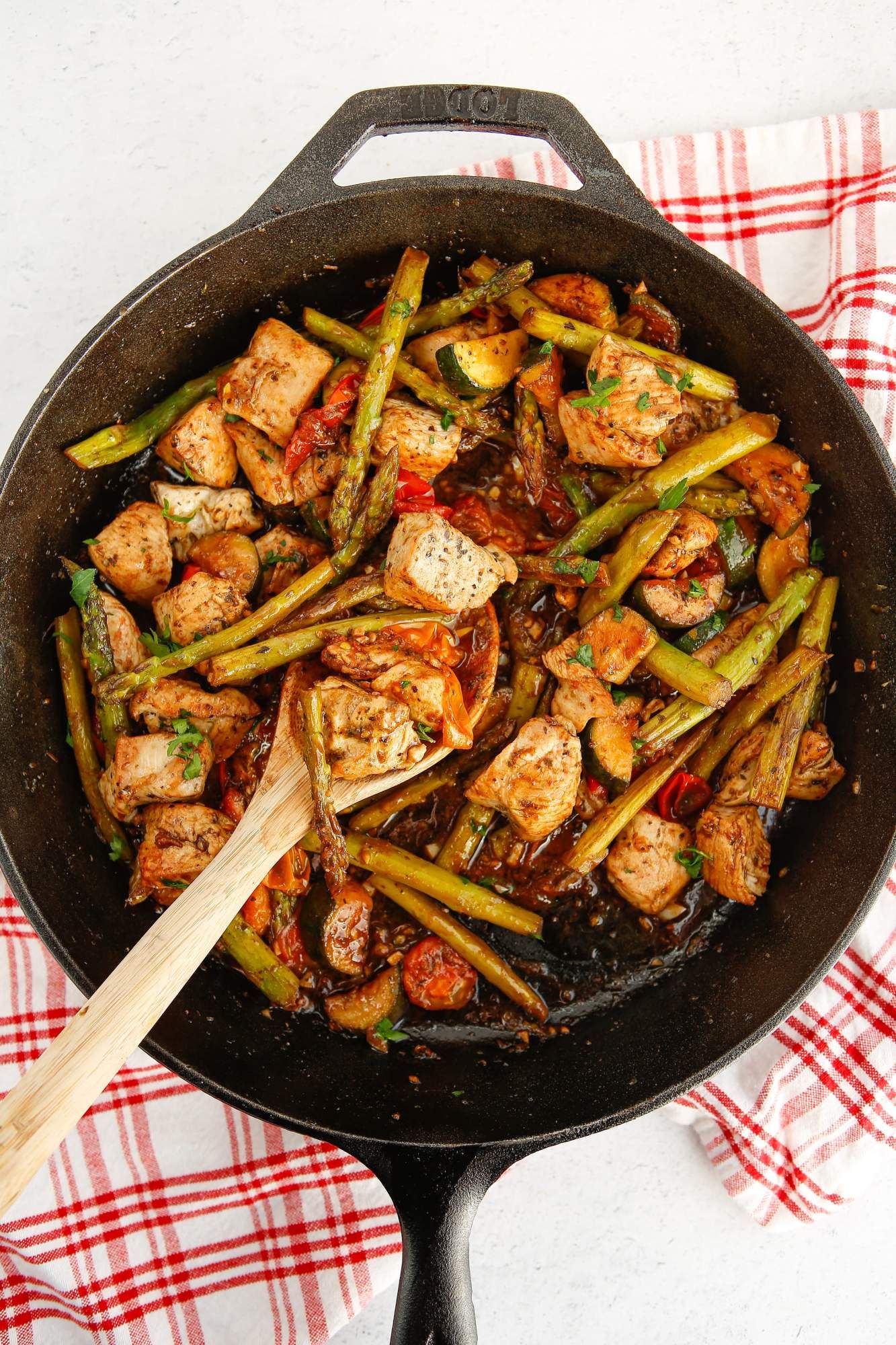 Chicken and vegetables with Italian seasoning, garlic, and burst cherry tomatoes in a cast iron skillet.