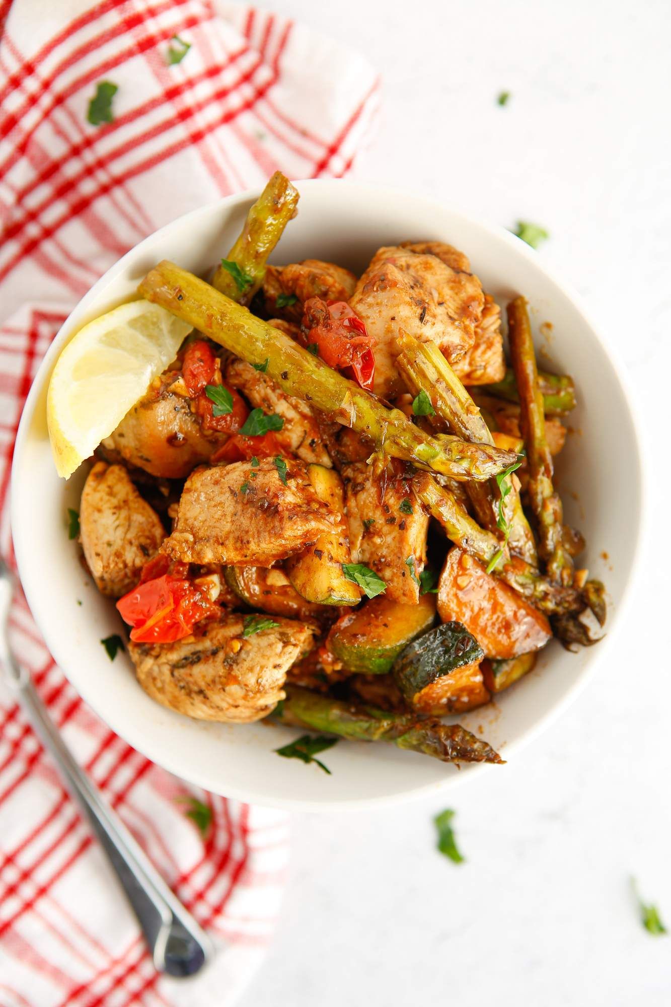 Italian chicken with asparagus, zucchini, tomatoes, garlic, and spices in a cast iron skillet with a red checkered napkin.