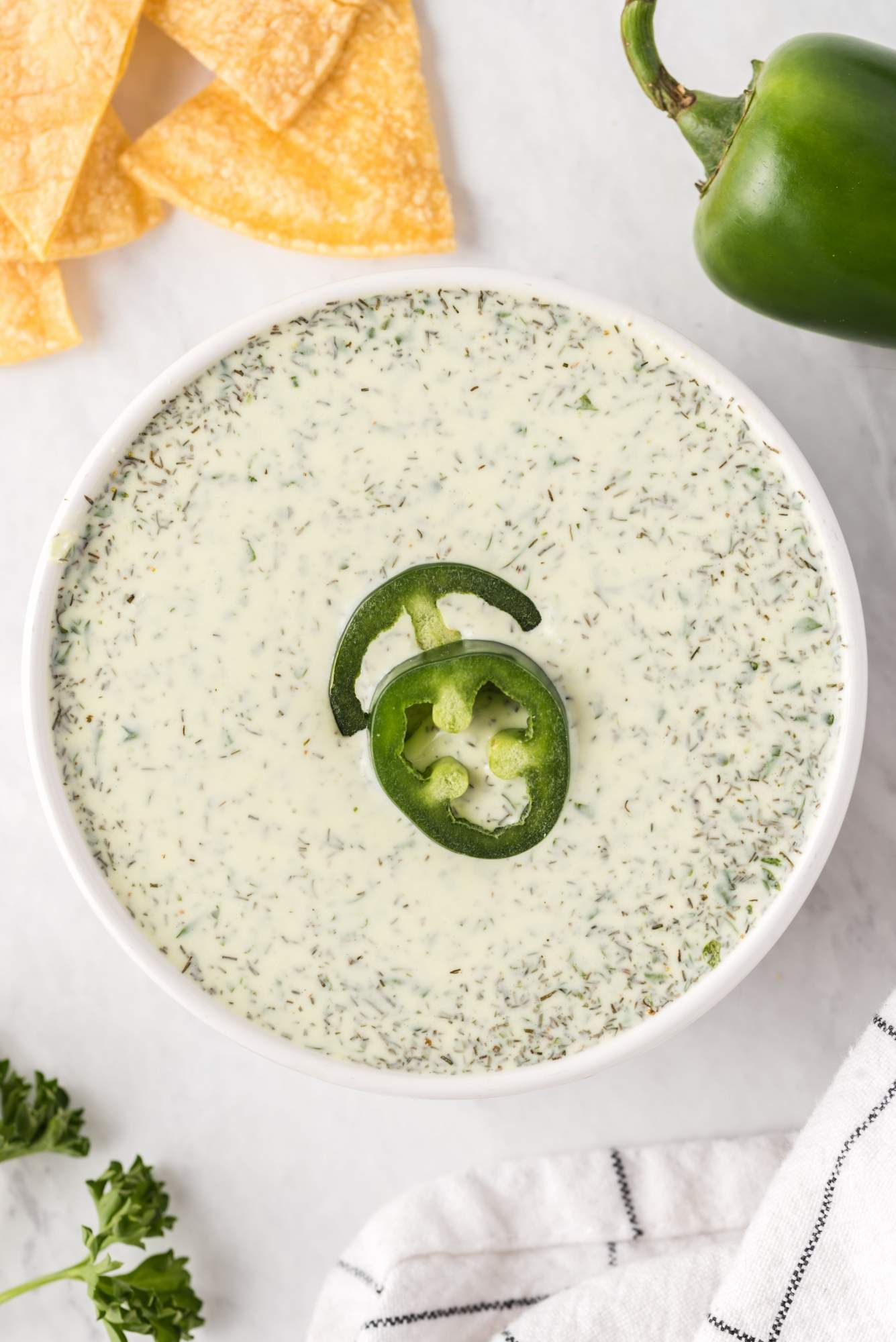 Spicy ranch dressing with jalapenos in a bowl with chips and sliced jalapenos on the side.