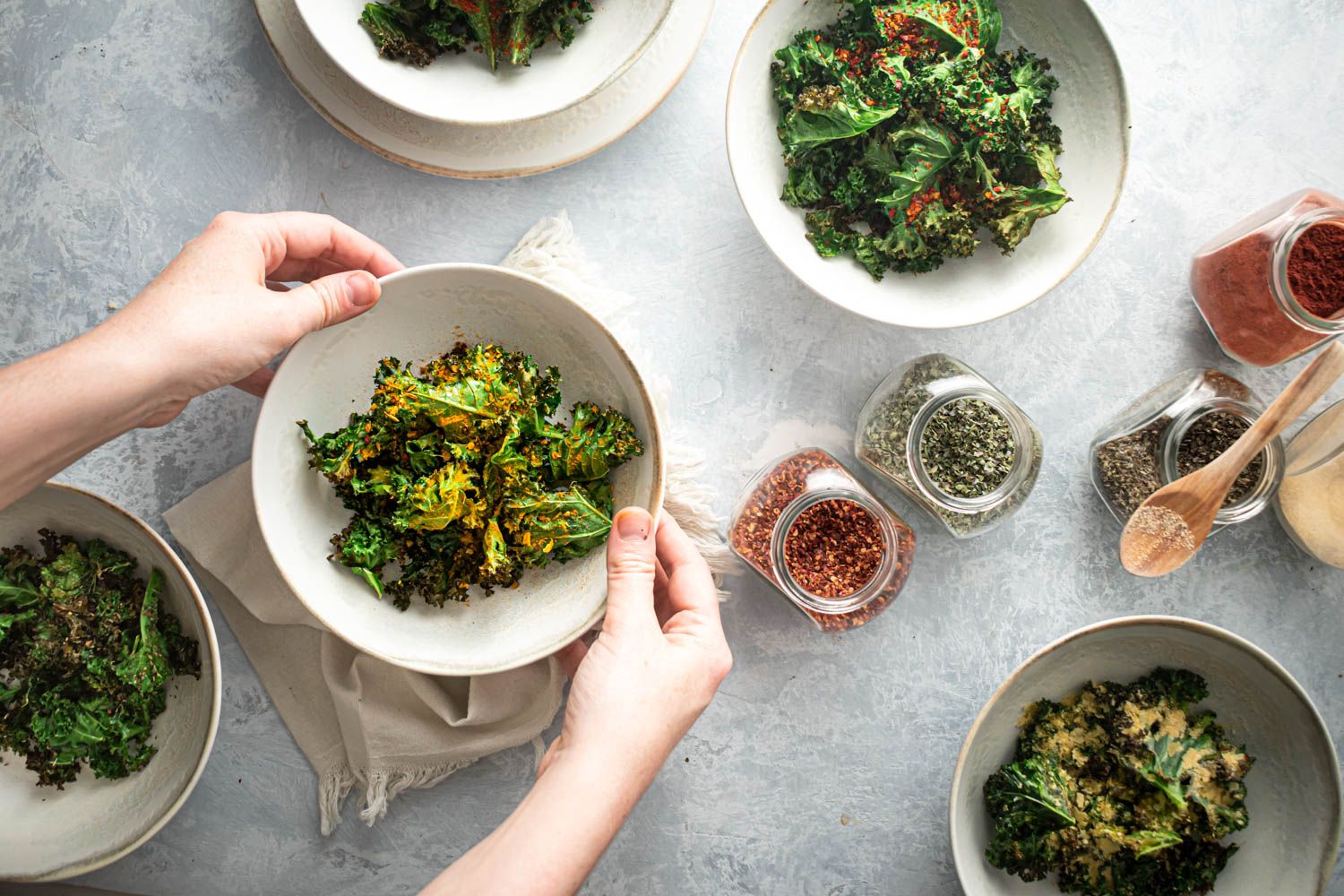 Baked kale chips in bowls with different seasoning blends.