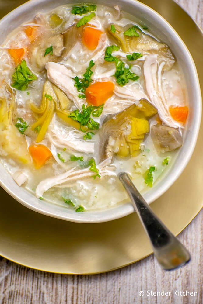 Lemon artichoke chicken soup with carrots, rice, onion, and parsley in a white bowl.