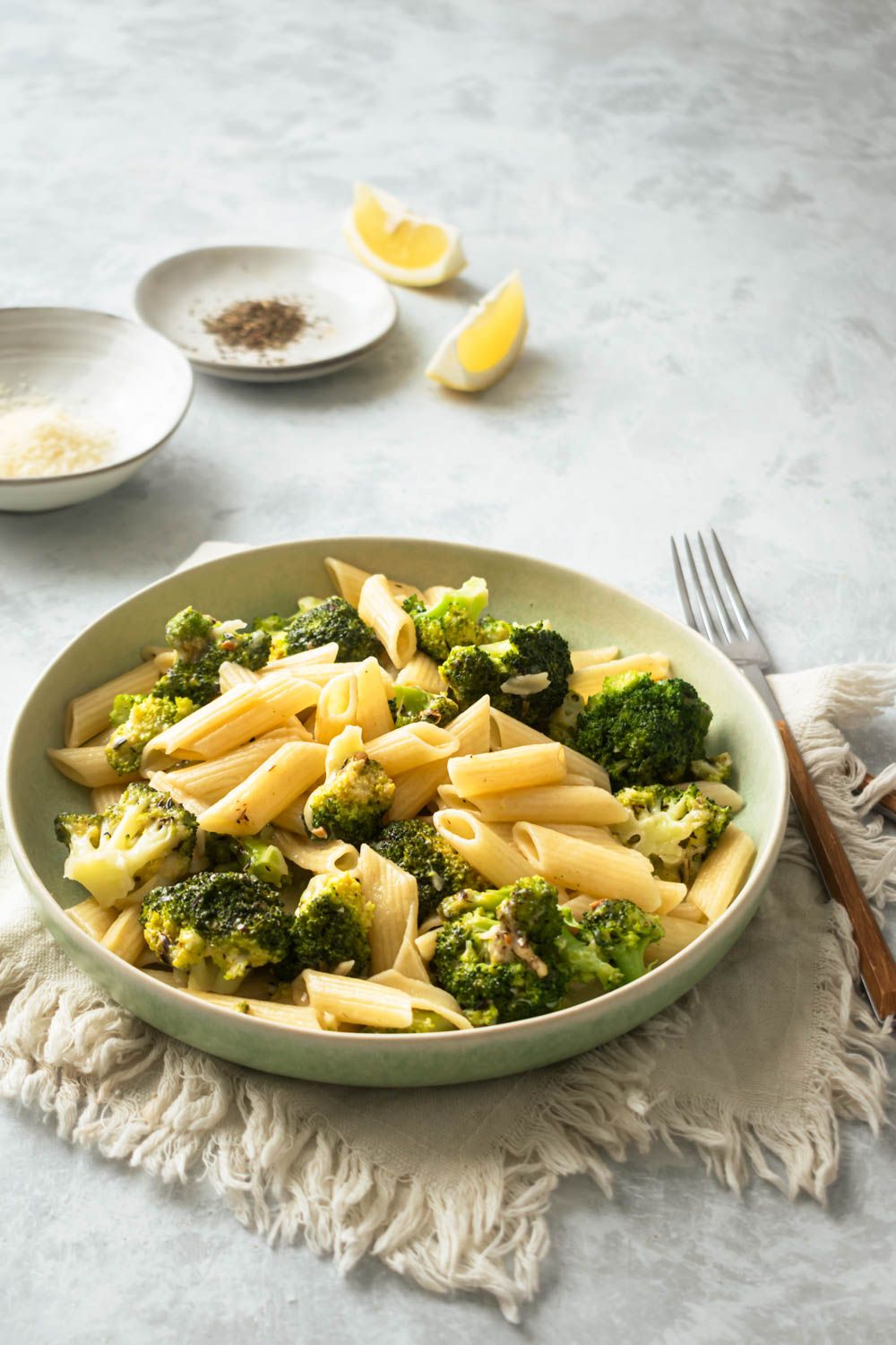 Pasta with broccoli, lemon, and garlic in a bowl with lemon and pepper on the side.