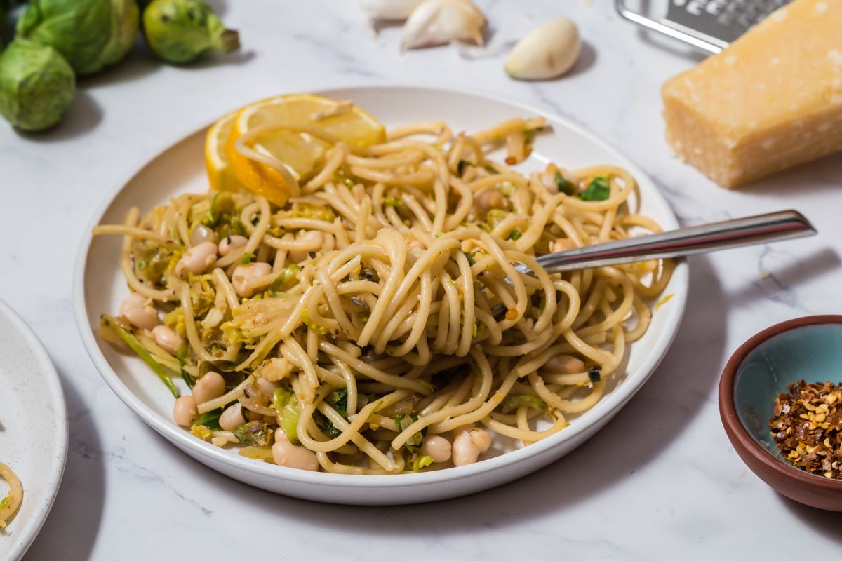 Pasta twirled on a fork with brussel sprouts, fresh lemon, white beans, and cheese. 