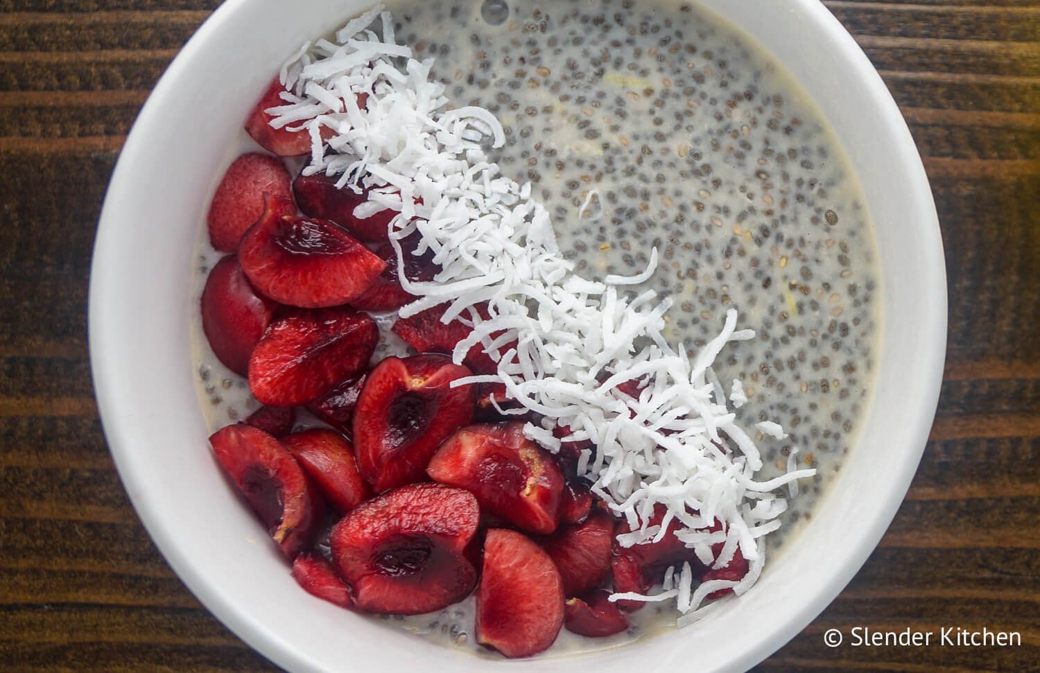 Lemon chia seed pudding with fresh cherries in a white bowl on wood background.