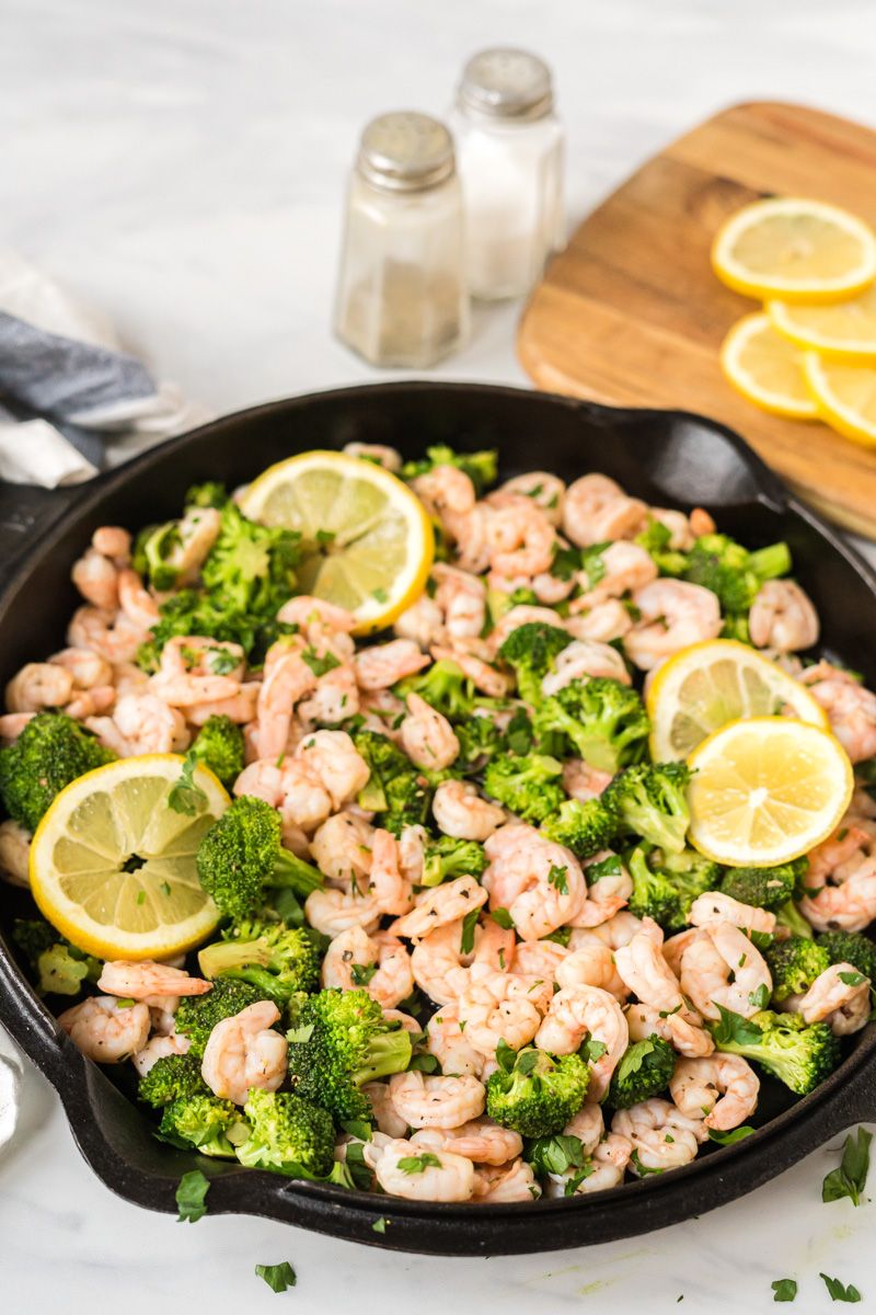 Shrimp cooked in a cast iron skillet with broccoli, lemon, and garlic with lemons and parsley on the side.