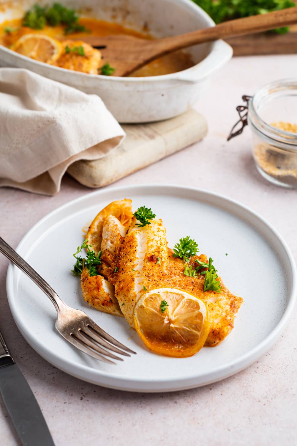 Tilapia with lemon pepper seasoning served on a plate with fresh lemon and parsley.