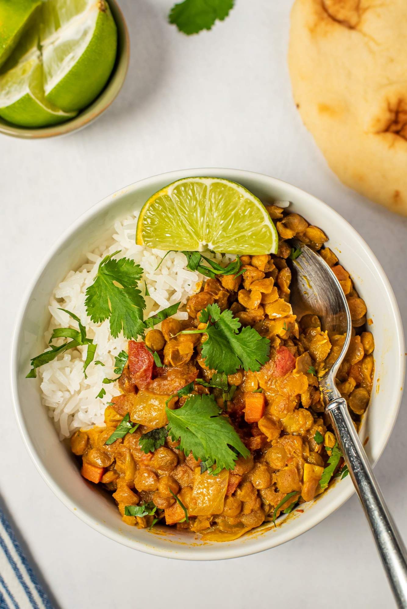 Coconut curried lentils in a bowl with white rice and cilantro with Naan bread on the side.