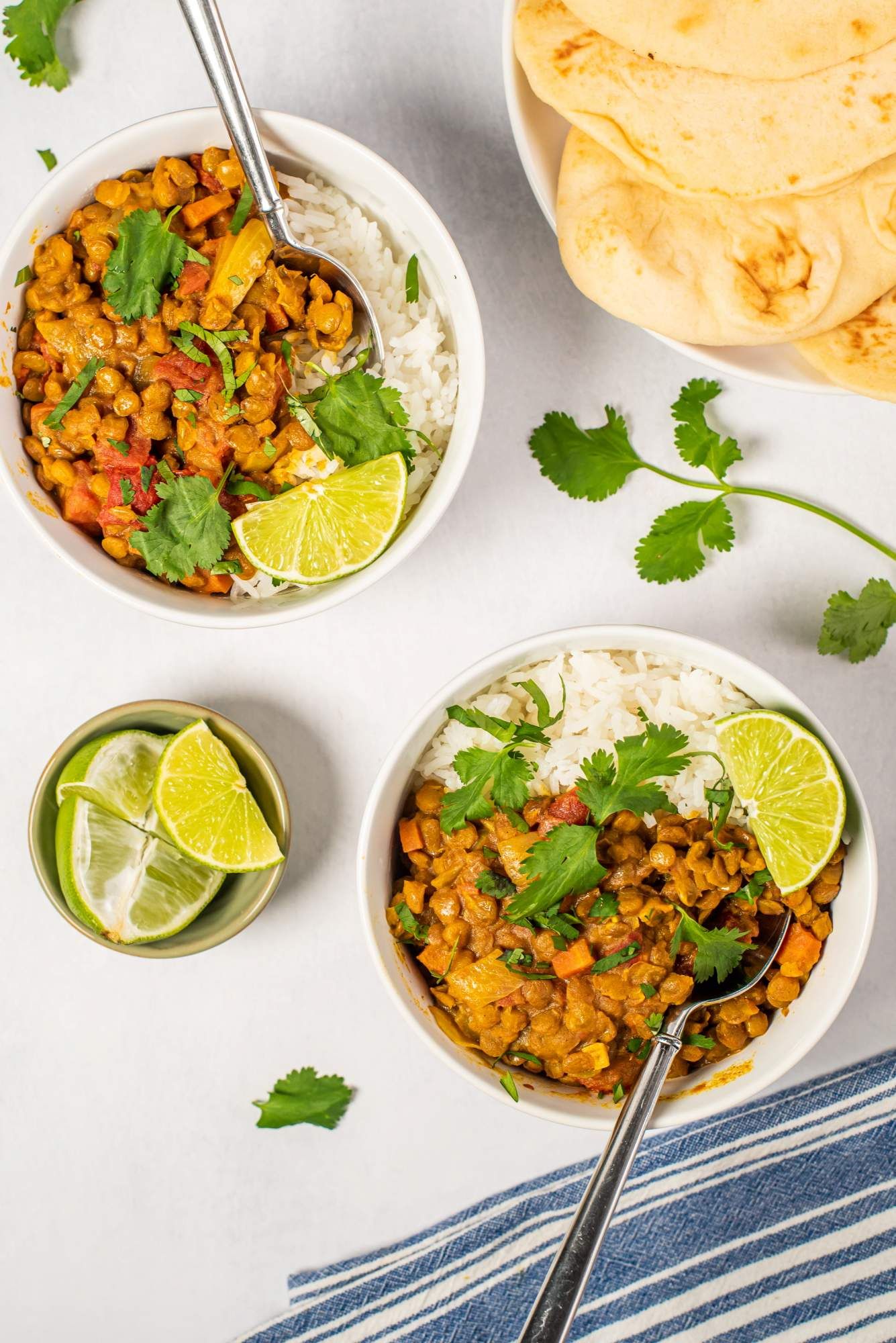 Curry lentil with coconut milk, carrots, and tomatoes in a bowl with fresh cilantro on a white counter.