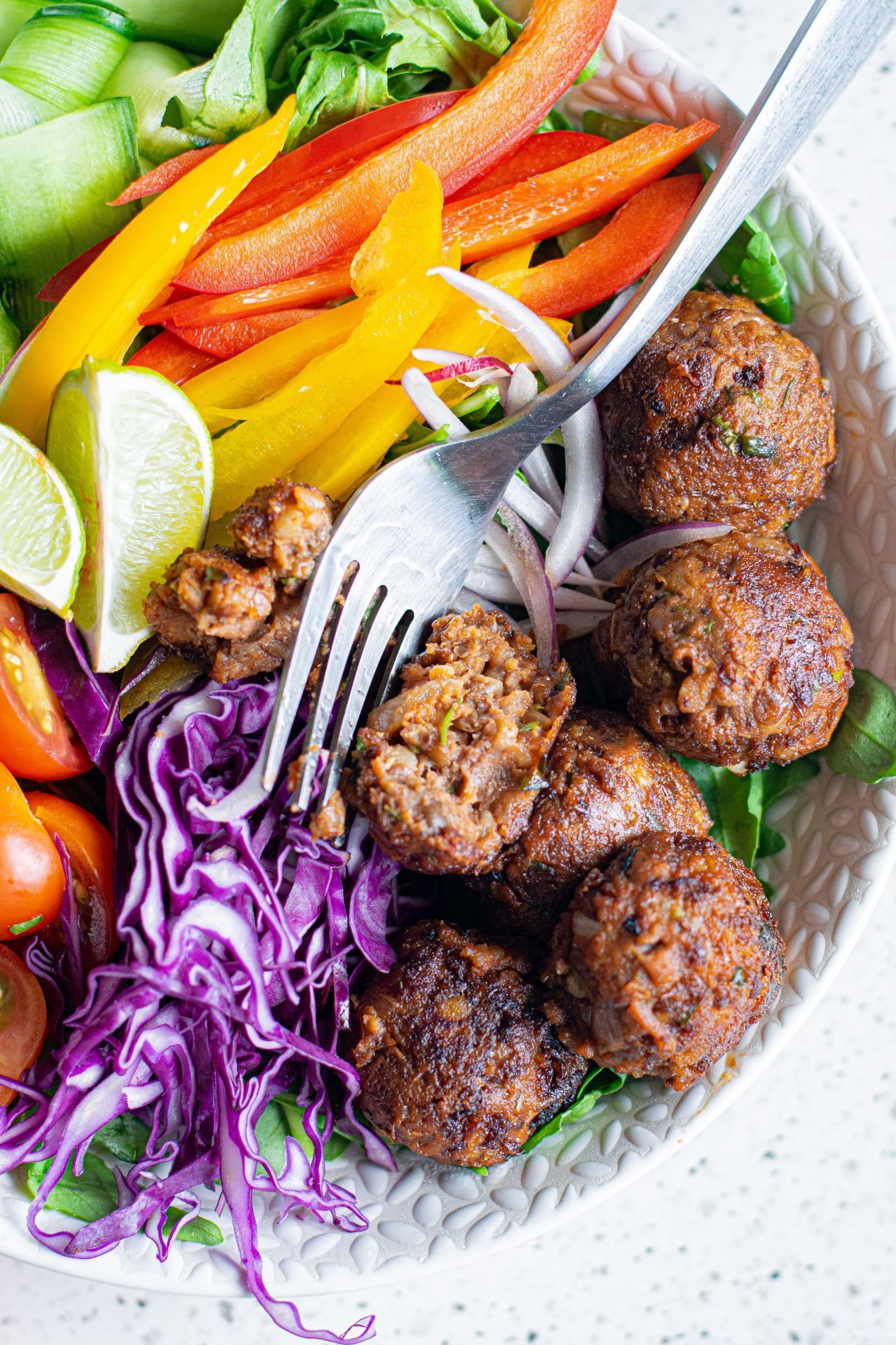 Vegetarian lentil meatballs served in a bowl with bell peppers, red cabbage, tomatoes, and greens served with a fork.